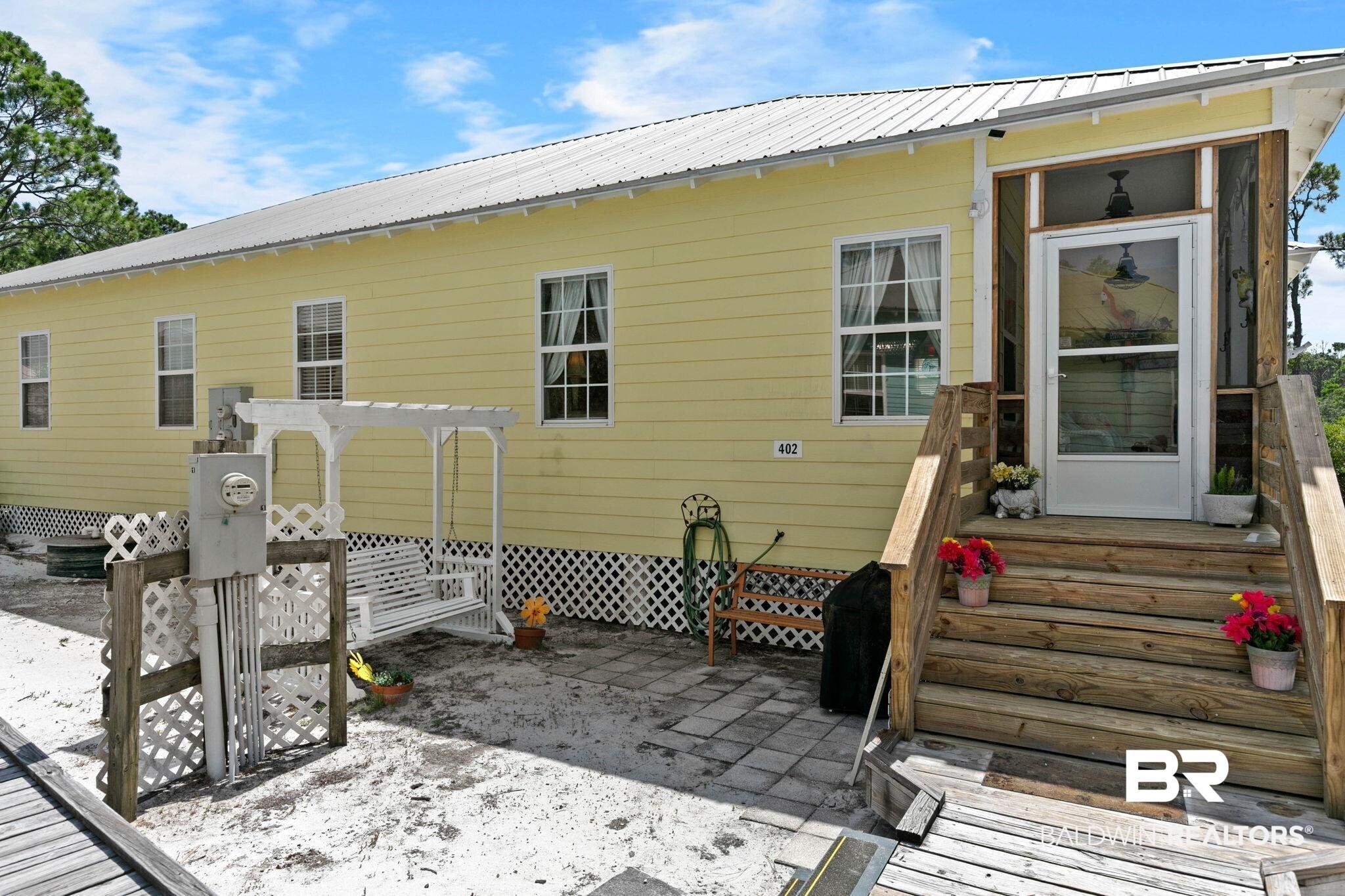 Image 3: Yellow siding exterior featuring a metal roof, an elevated wood-decked entry, and a screened front porch