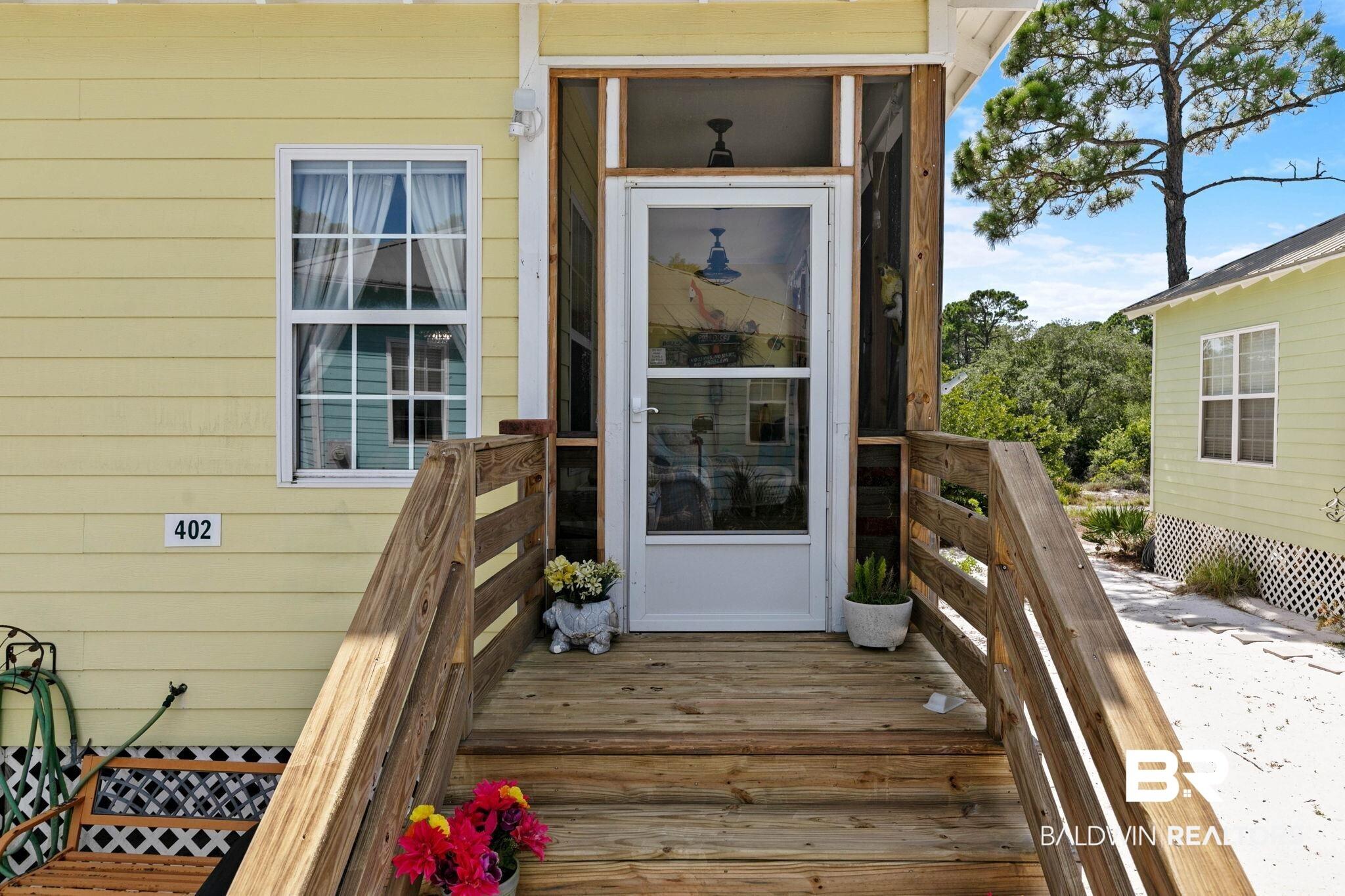 Image 4: Yellow siding exterior featuring a screened entry porch with a clear glass storm door, wood steps, and wood railings