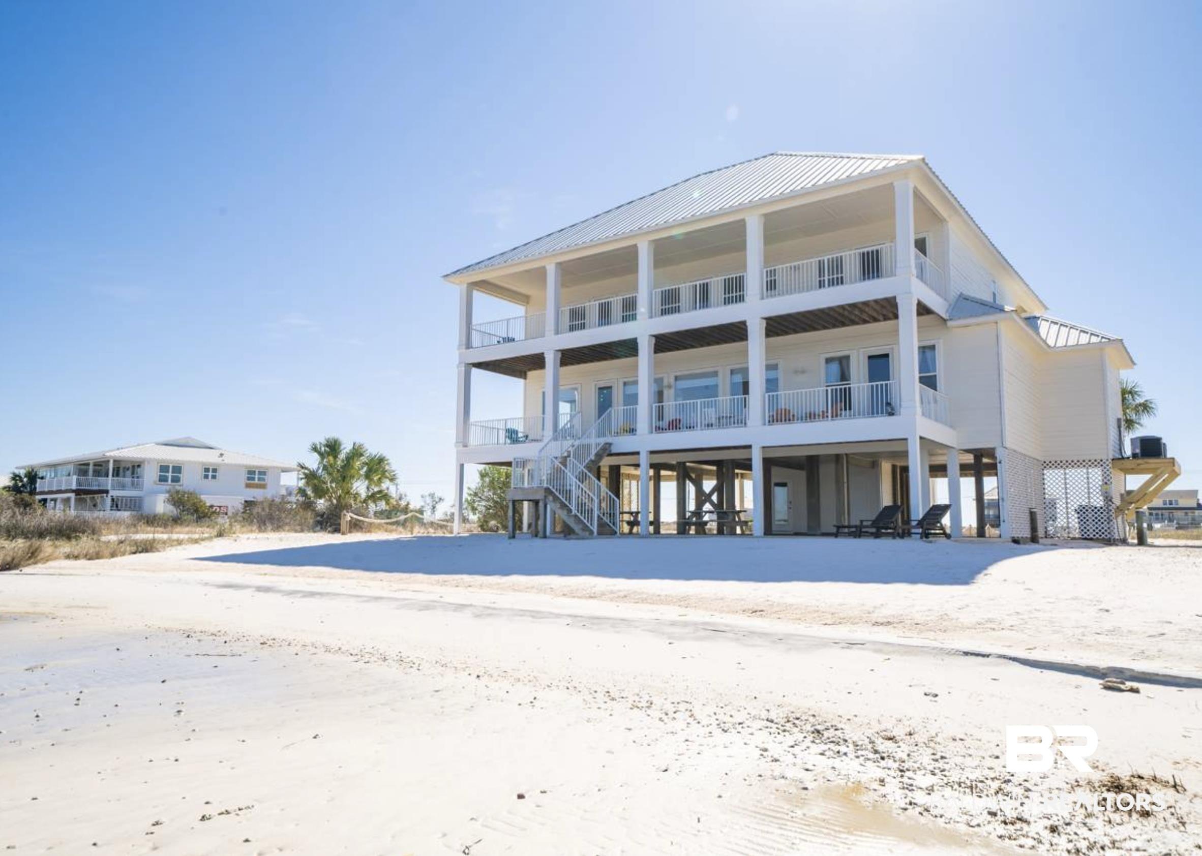 Image 2: Elevated coastal residence featuring multiple covered balconies, a metal roof, and direct access to a sandy beach