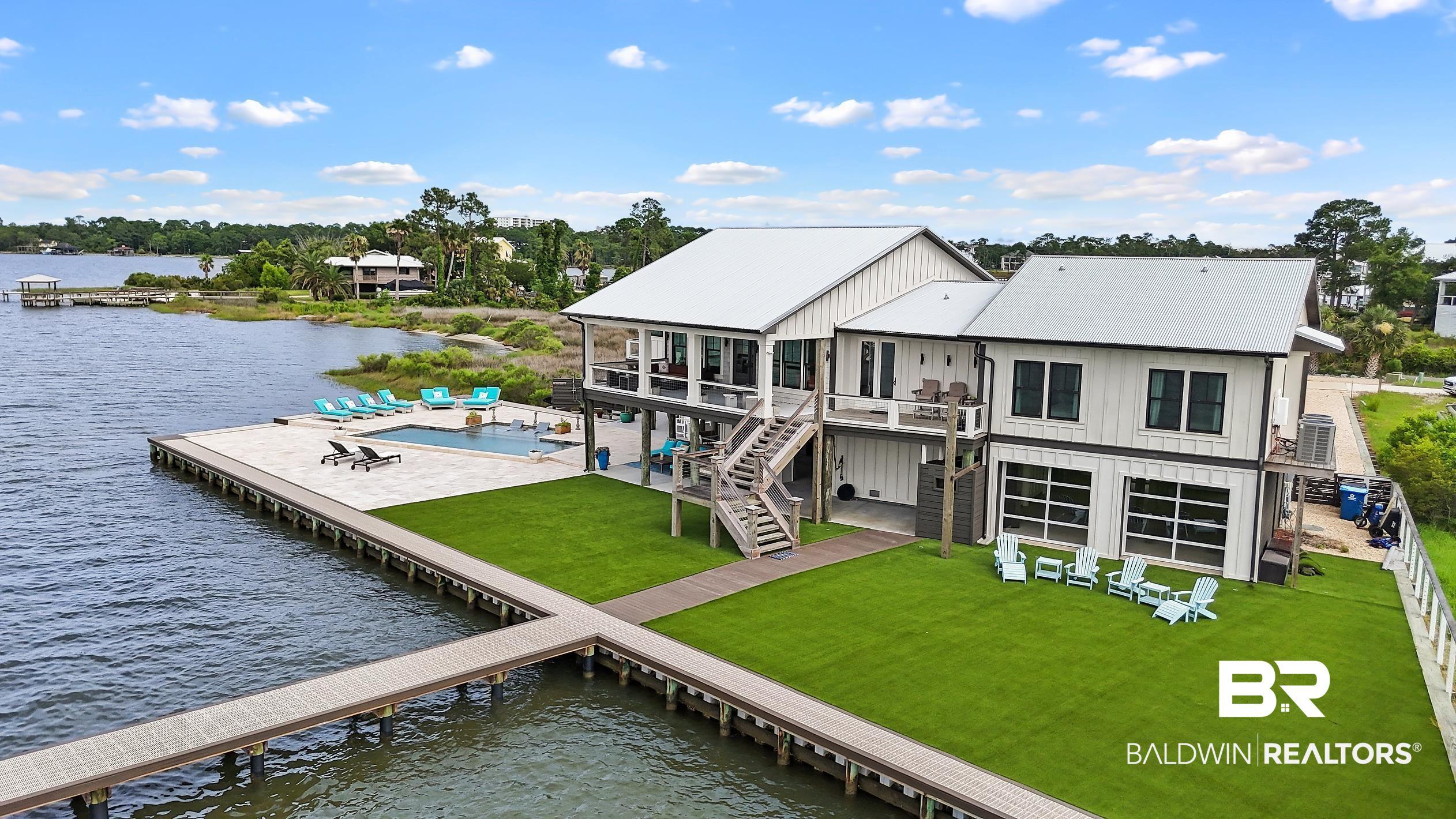 Image 1: Waterfront residence featuring a private dock, expansive waterside patio, in-ground swimming pool, artificial turf lawn, and a two-story exterior with multiple balconies