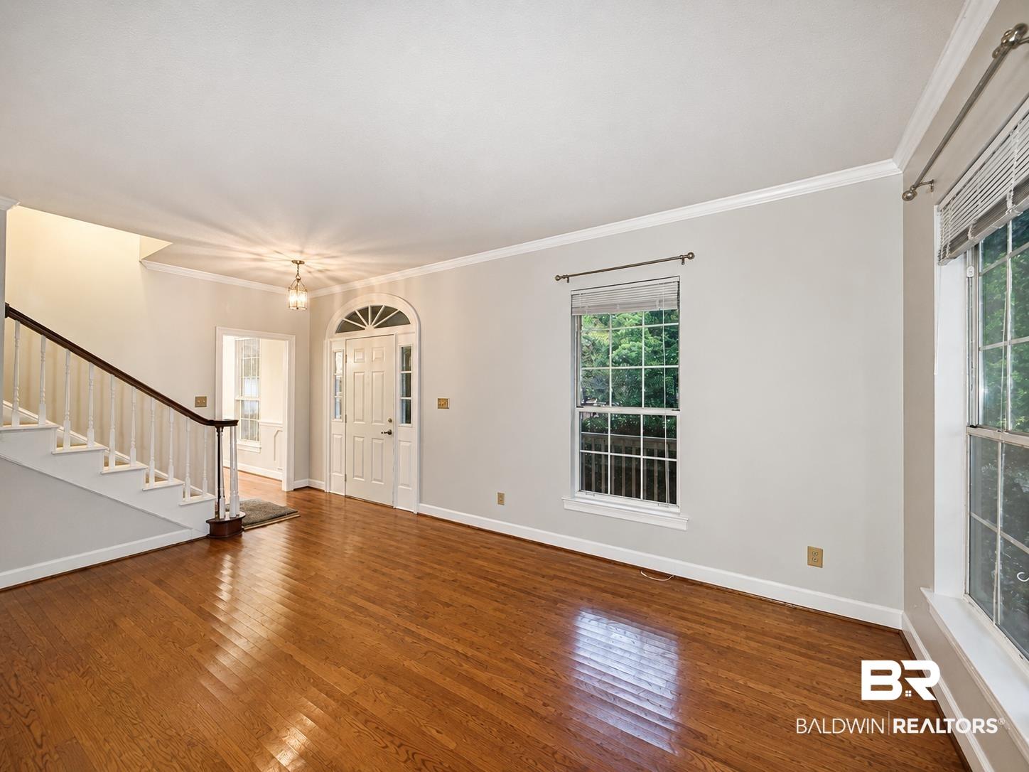 Image 4: Foyer entry featuring hardwood flooring, a white paneled front door with an arched transom, a pendant light fixture, and a staircase with white balusters and a dark wood handrail