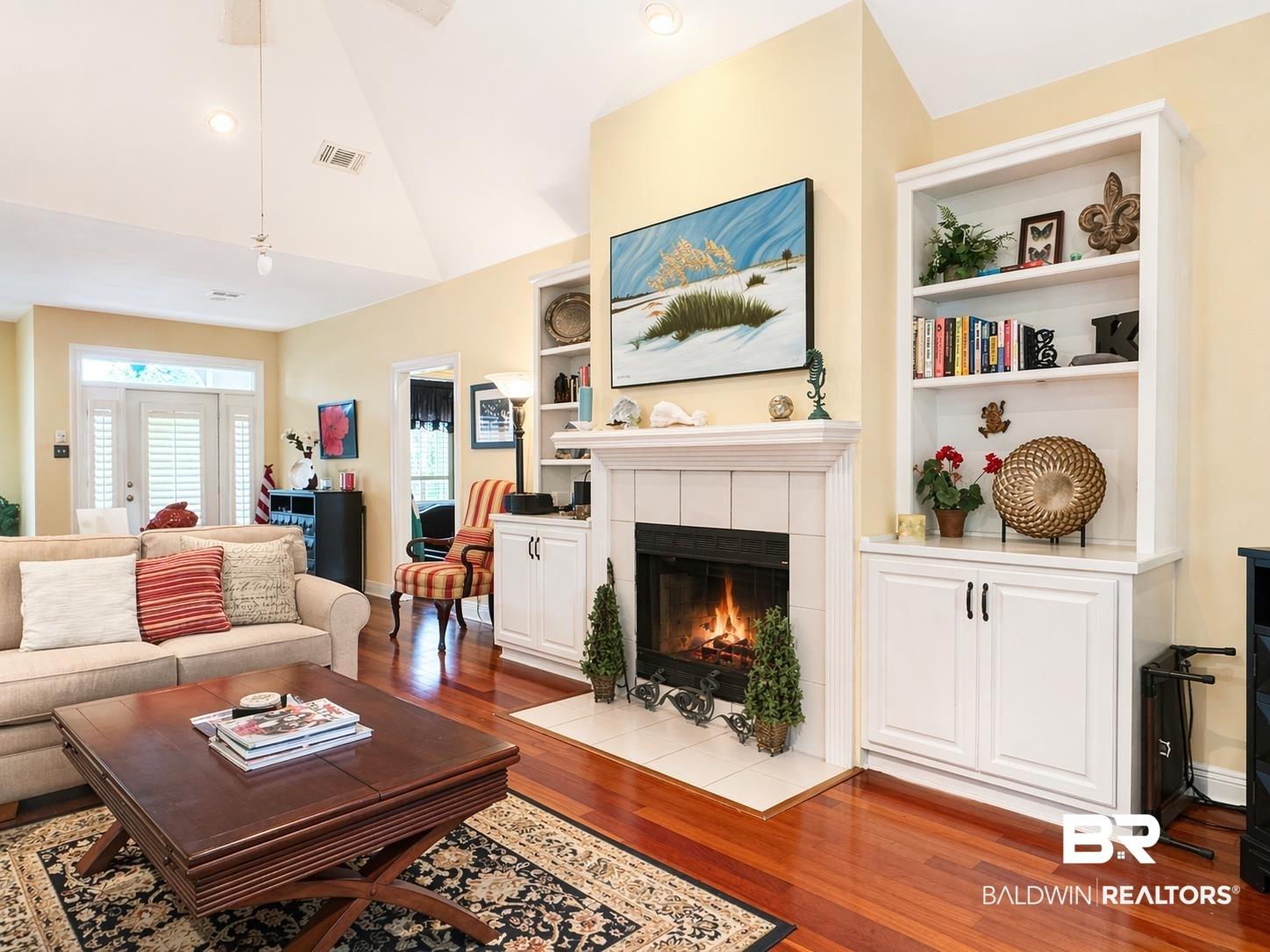 Image 2: Living area featuring dark wood-style flooring, built in shelves, a tiled fireplace, ceiling fan, and vaulted ceiling
