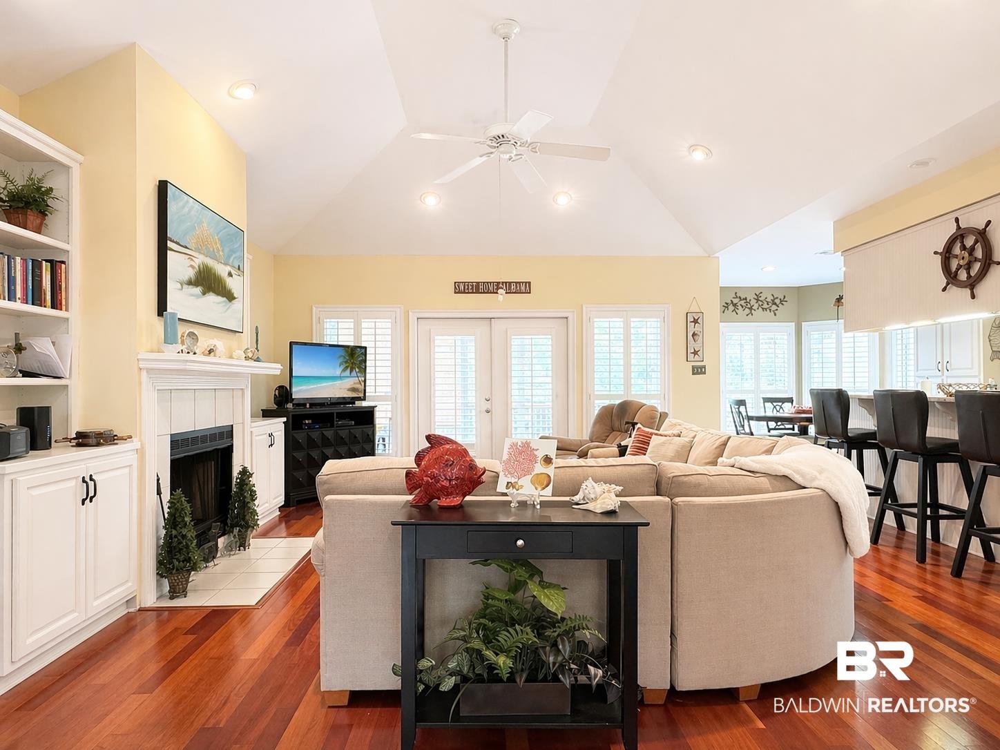 Image 4: Living area featuring ceiling fan, a tiled fireplace, hardwood / wood-style floors, french doors, and lofted ceiling