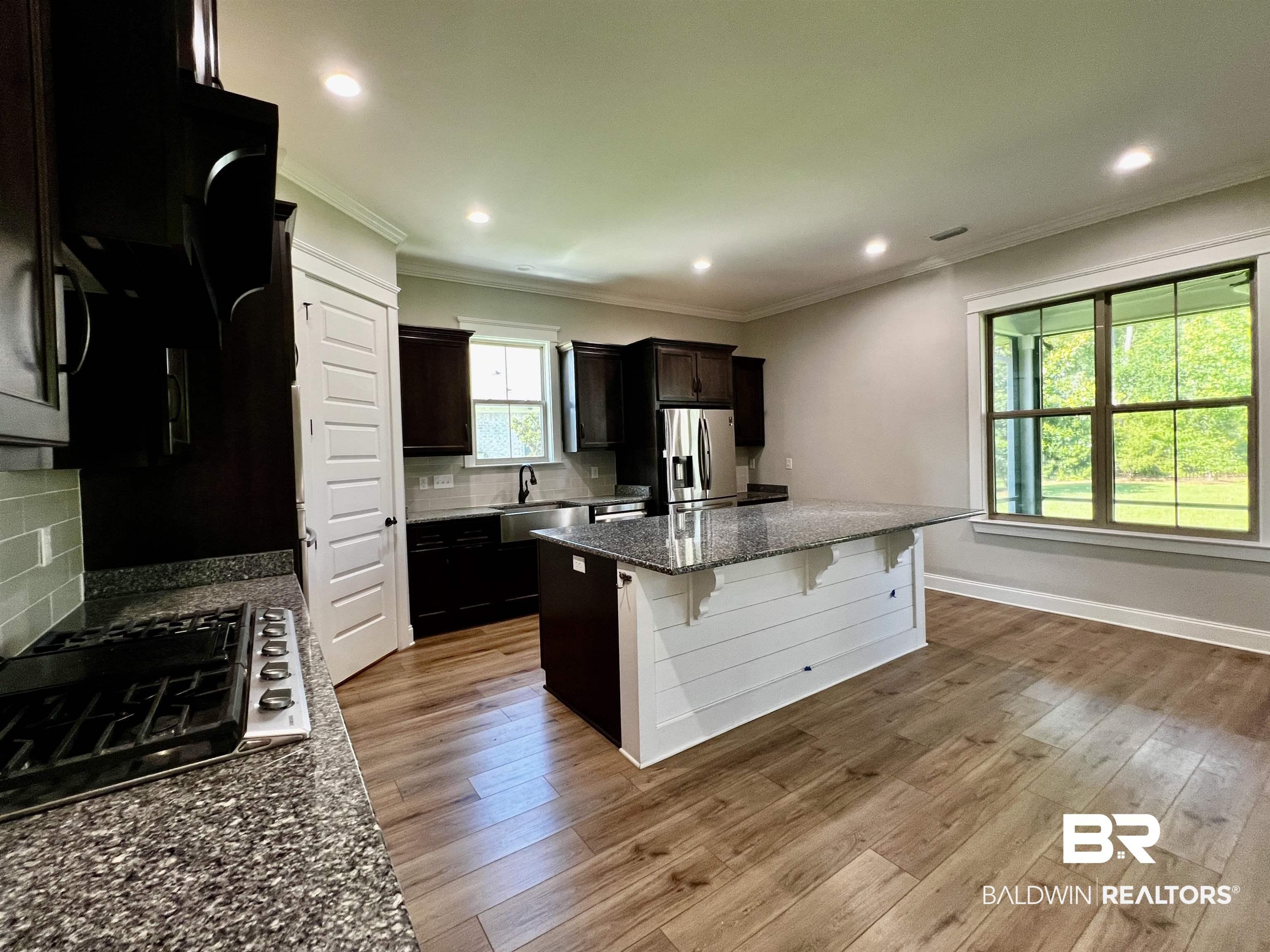 Image 4: Kitchen featuring wood-finish flooring, dark wood cabinetry, light-toned backsplash, recessed lighting, and a center island with a white shiplap base and granite-style countertop