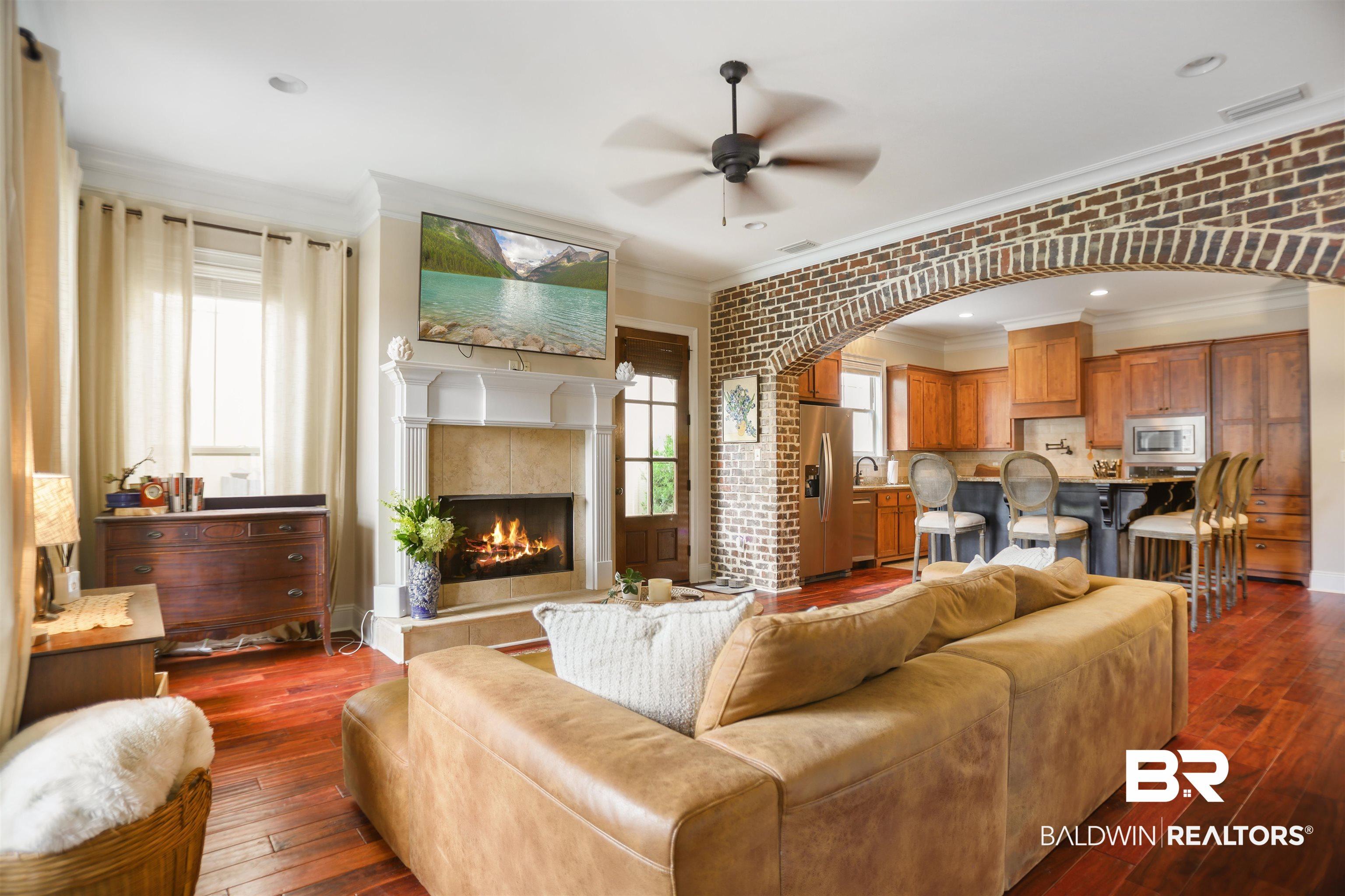Image 4: Living area featuring wood-finish flooring, a fireplace with a stone surround and ornate mantel, and a brick archway leading to the kitchen