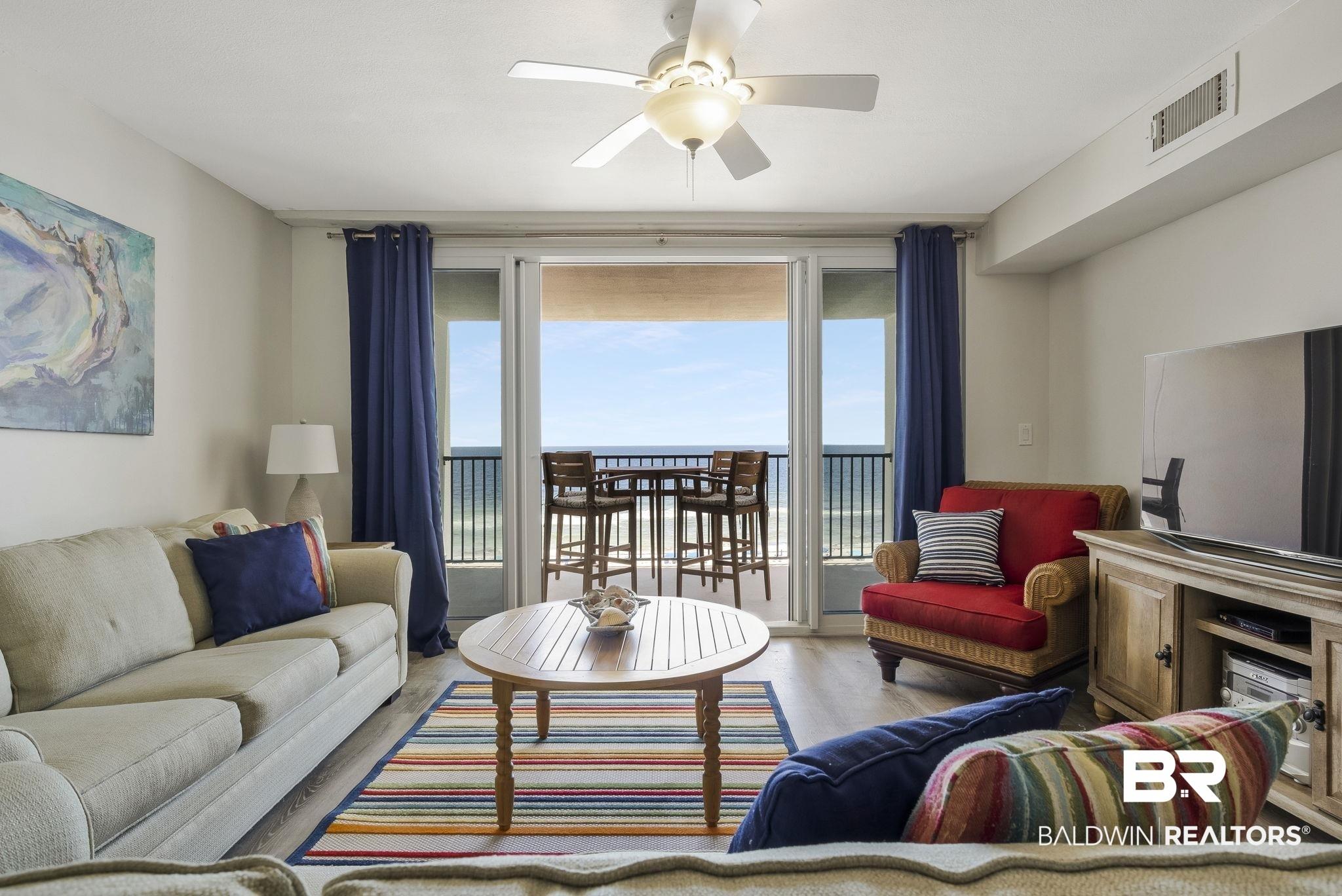 Image 3: Spacious living area featuring light wood-finish flooring, a ceiling fan, and direct balcony access