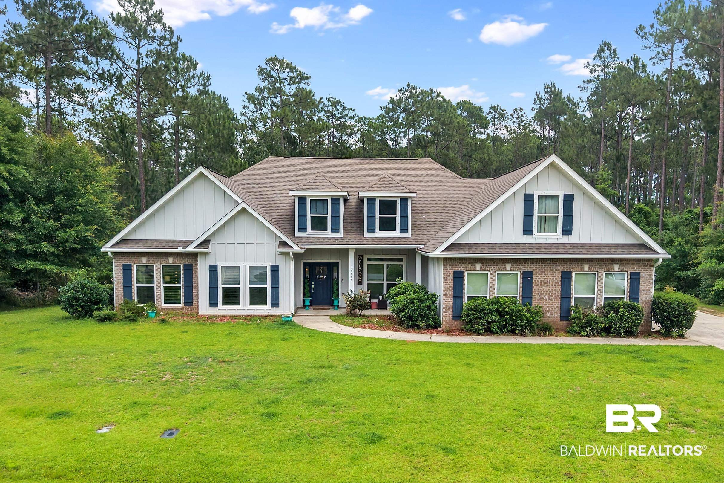 Image 2: Expansive front lawn with a traditional-style residence featuring a brick and vertical siding facade, dark shutters, a front entry with a dark door, and a multi-gabled roofline