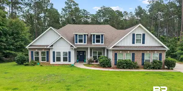 Image 2: Expansive front lawn with a traditional-style residence featuring a brick and vertical siding facade, dark shutters, a front entry with a dark door, and a multi-gabled roofline