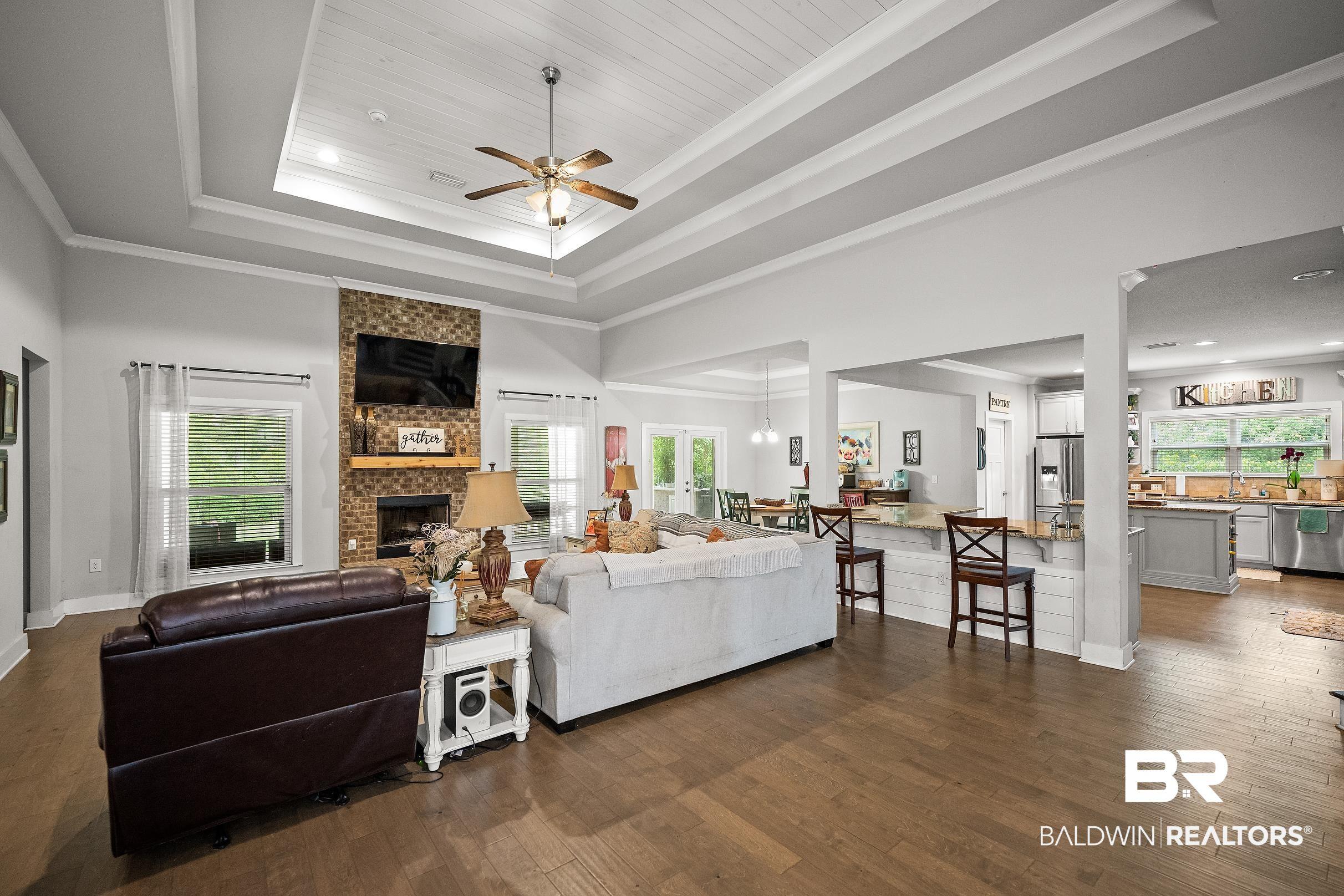 Image 3: Spacious living area featuring wood-finish flooring, a tray ceiling with shiplap detail, and a ceiling fan