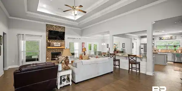 Image 3: Spacious living area featuring wood-finish flooring, a tray ceiling with shiplap detail, and a ceiling fan
