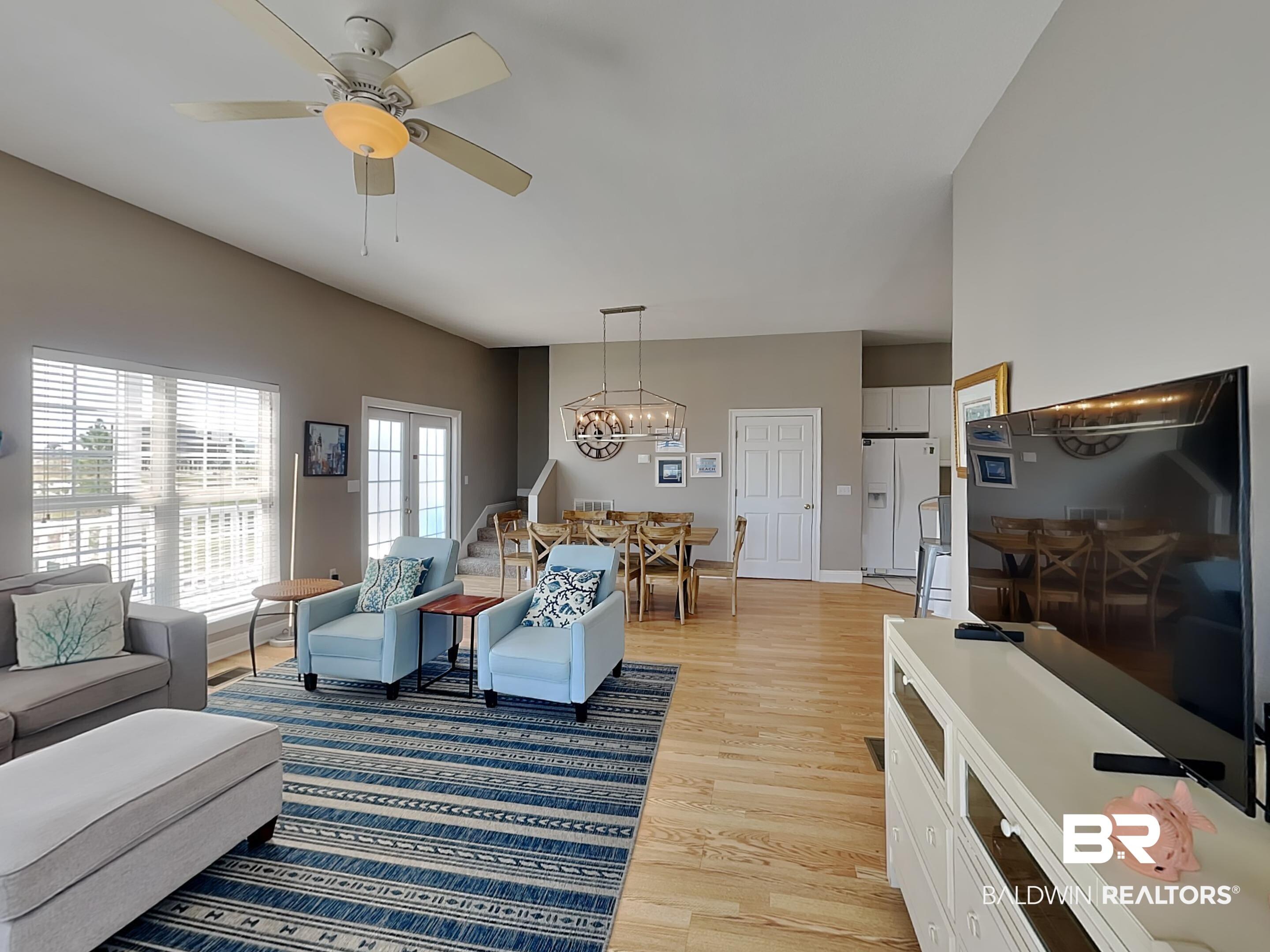 Image 4: Open-concept living area featuring light wood-finish flooring, a vaulted ceiling, and ample natural light from large windows with blinds