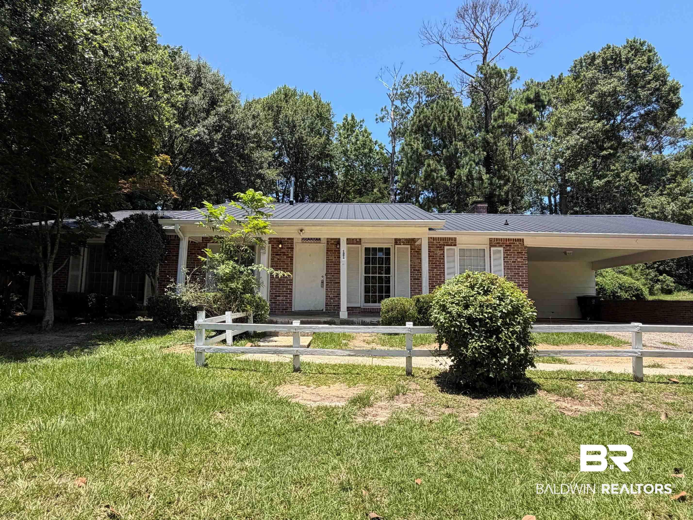 Image 1: Brick ranch-style residence featuring a dark metal roof, white porch columns, and a covered carport