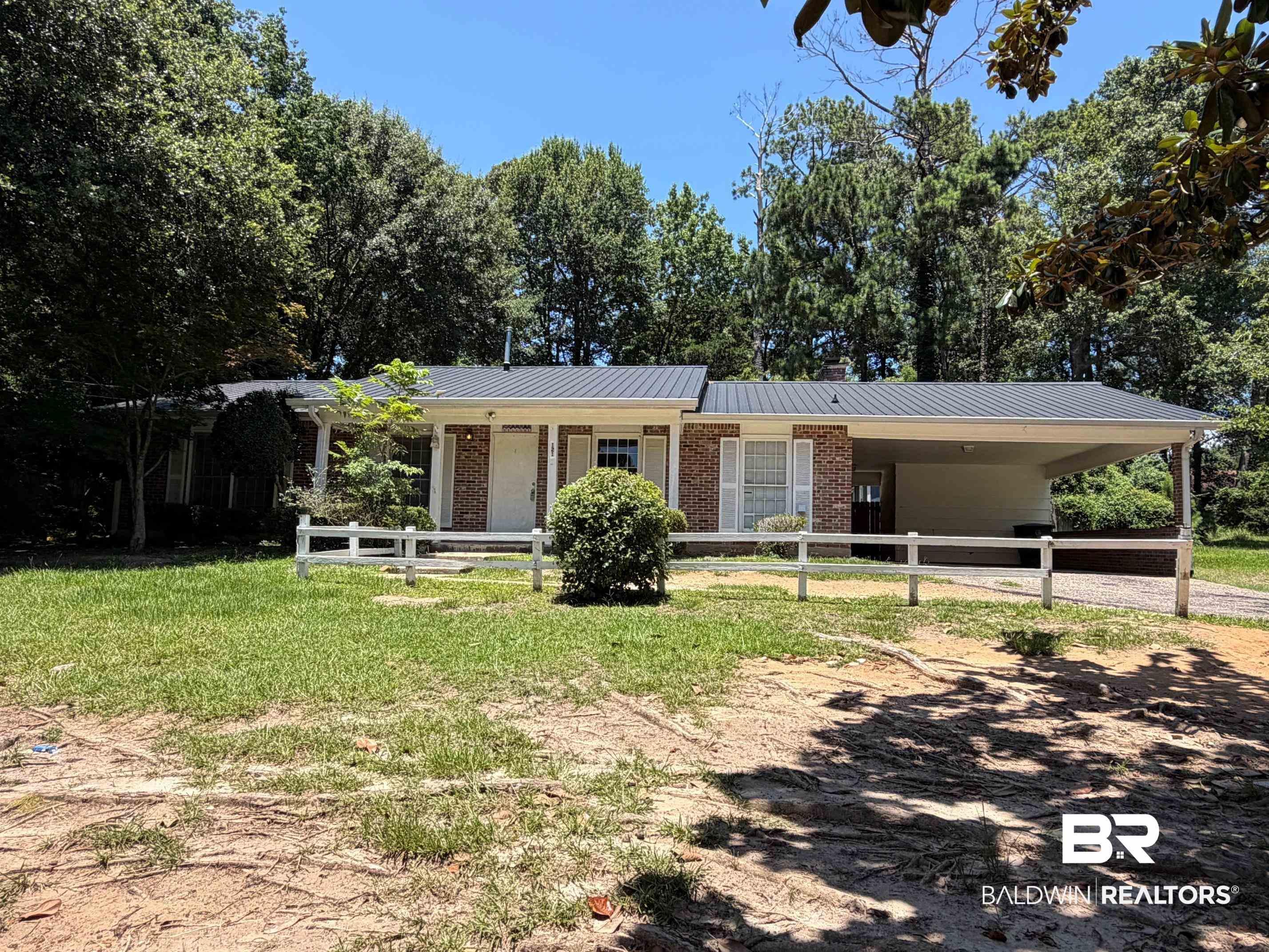 Image 4: Brick ranch-style residence featuring a metal roof, an attached carport, and a white picket fence
