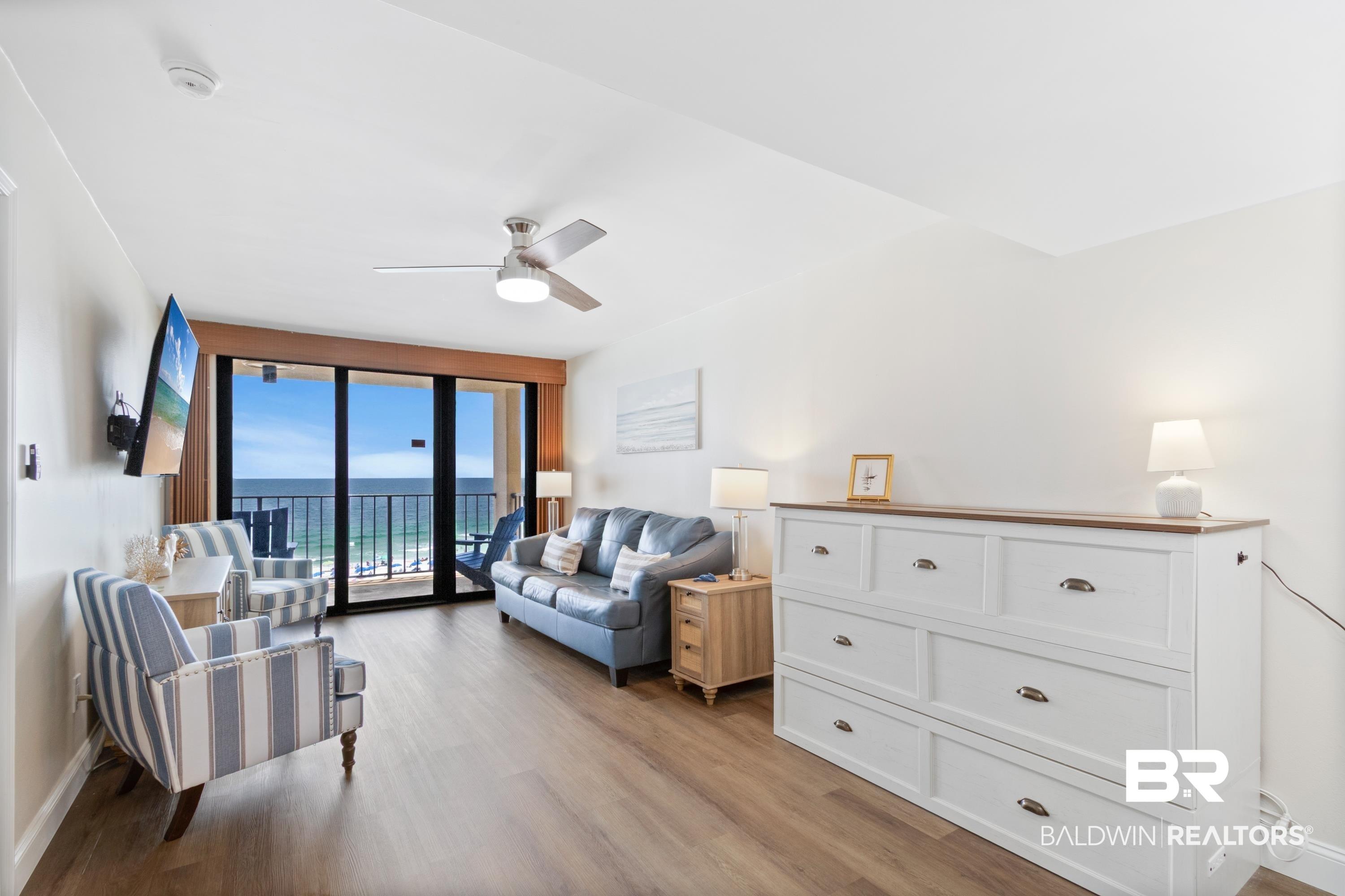 Image 4: Living area featuring wood-finish flooring, a ceiling fan with integrated lighting, and direct balcony access through sliding glass doors