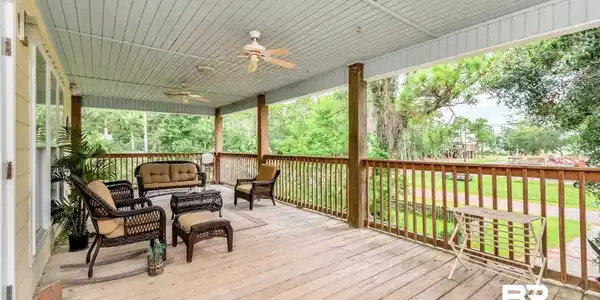 Image 3: Expansive covered wood deck featuring a beadboard ceiling, two ceiling fans, and a wood railing