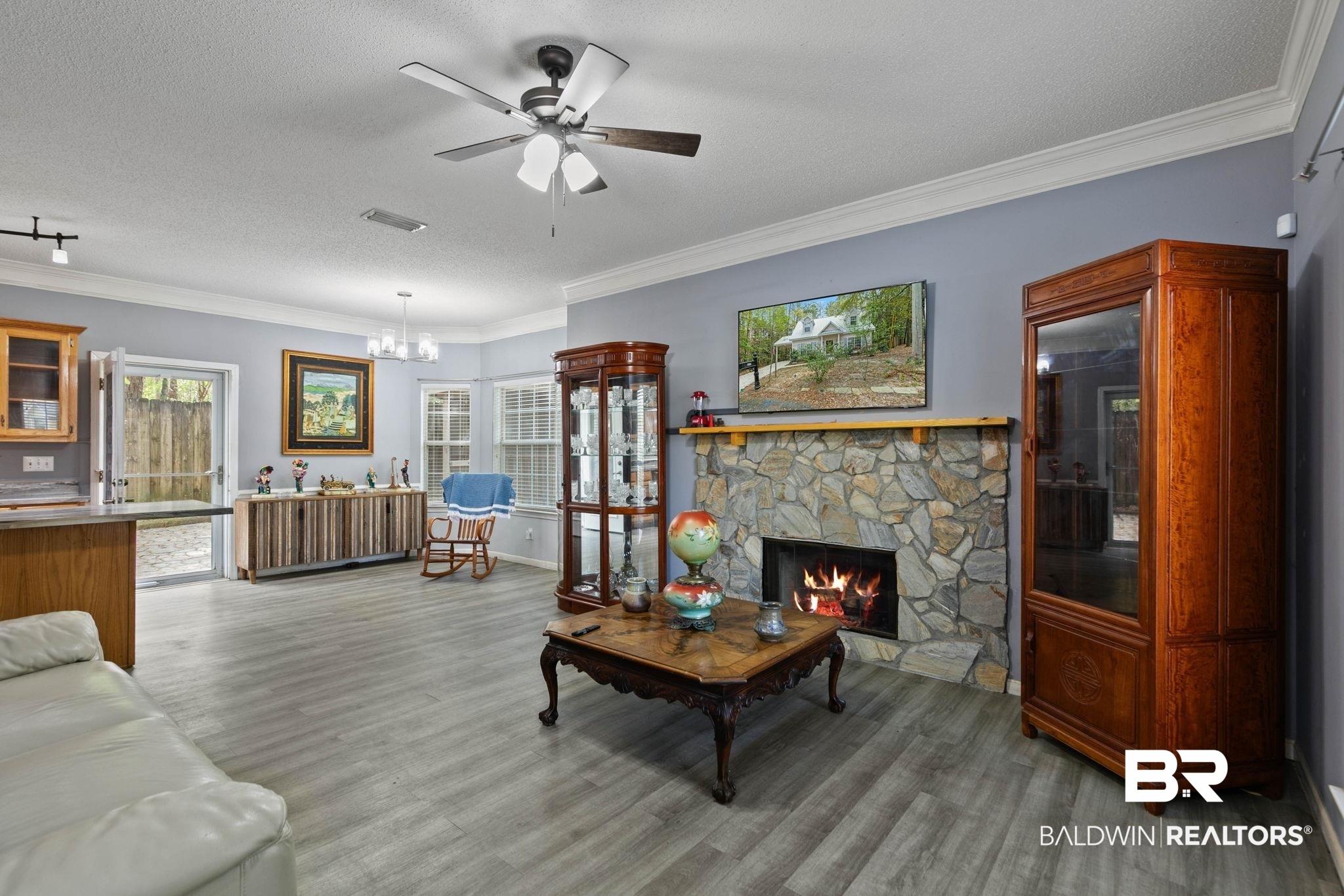 Image 4: Living area featuring a textured ceiling, crown molding, ceiling fan, light wood-style flooring, and a stone fireplace