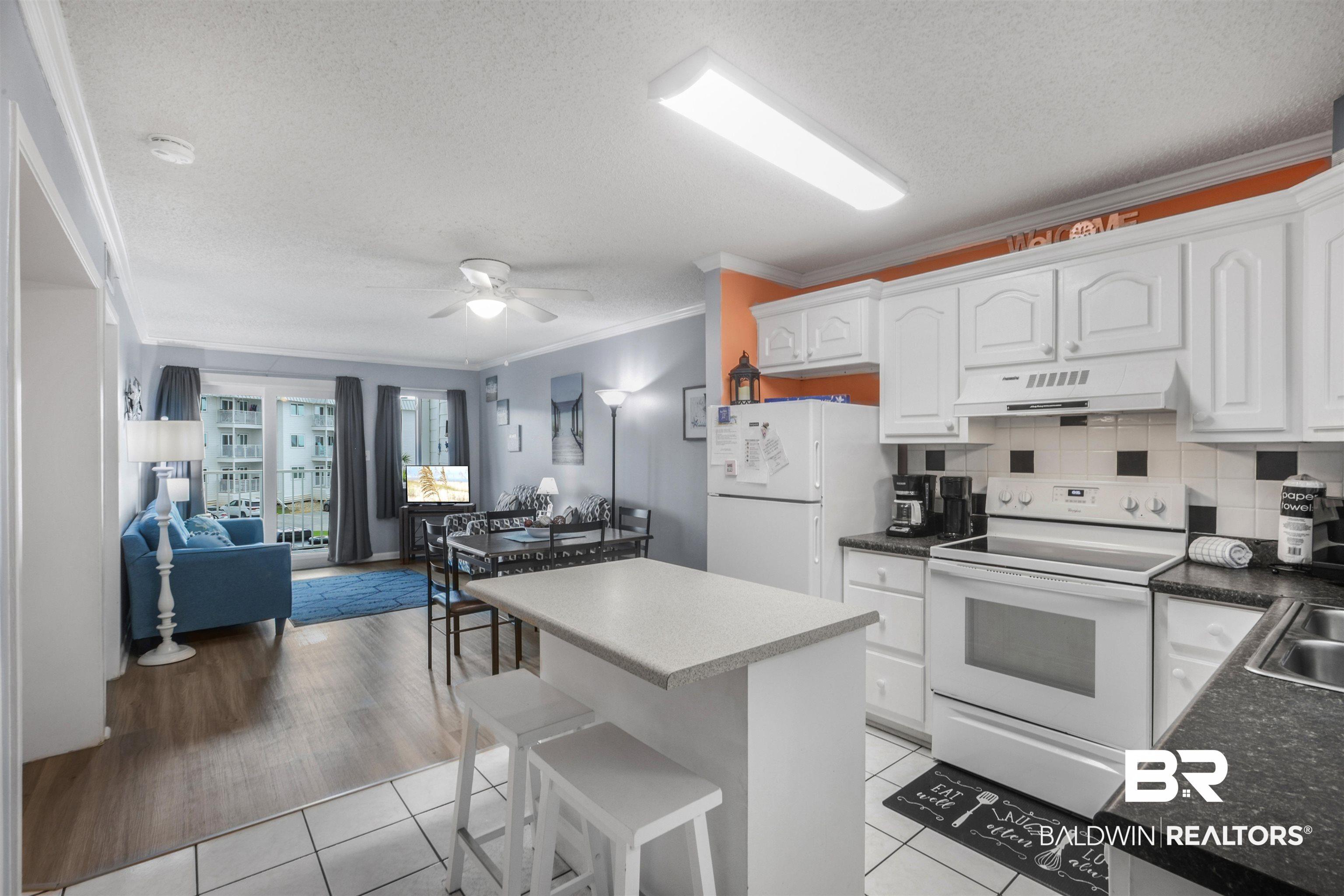 Image 2: Open-concept kitchen and living area featuring white cabinetry, a kitchen island with seating, a white appliance suite, and wood-finish flooring in the living space