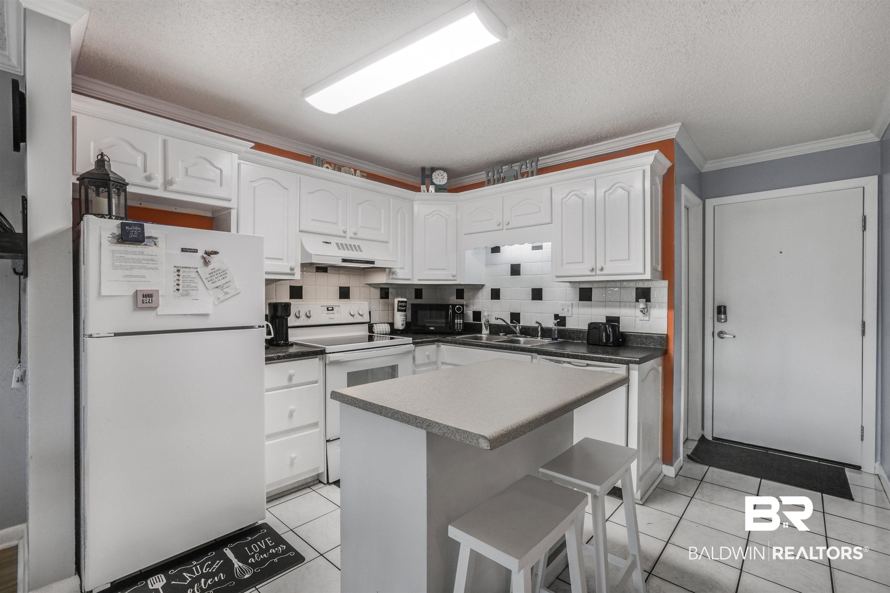 Image 3: Kitchen featuring white cabinetry, black countertops, and a white tile floor