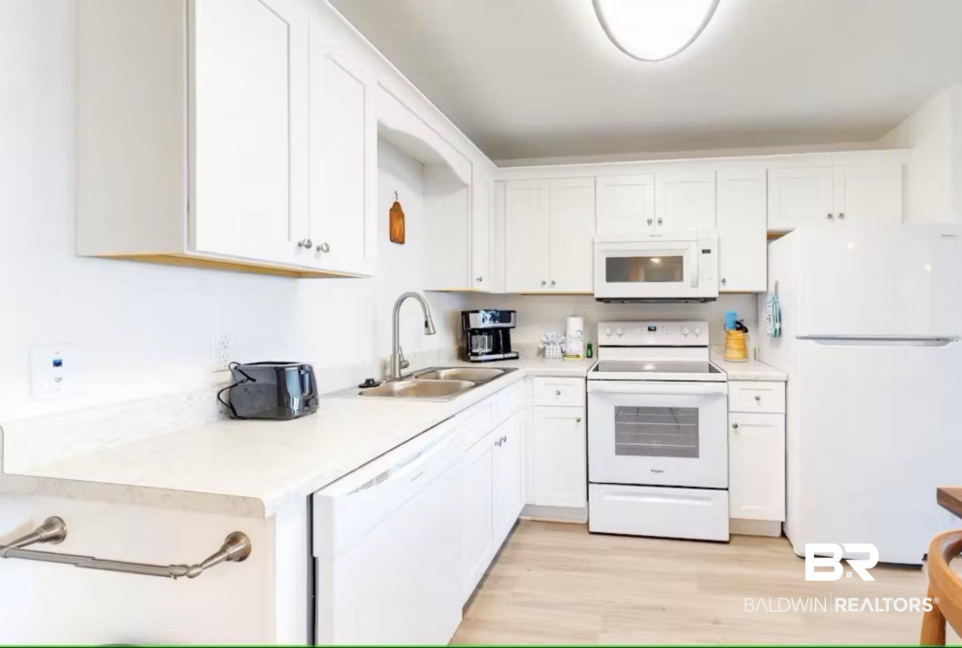 Image 3: Kitchen featuring white cabinetry, light-toned countertops, wood-finish flooring, stainless steel sink with gooseneck faucet, and white appliances