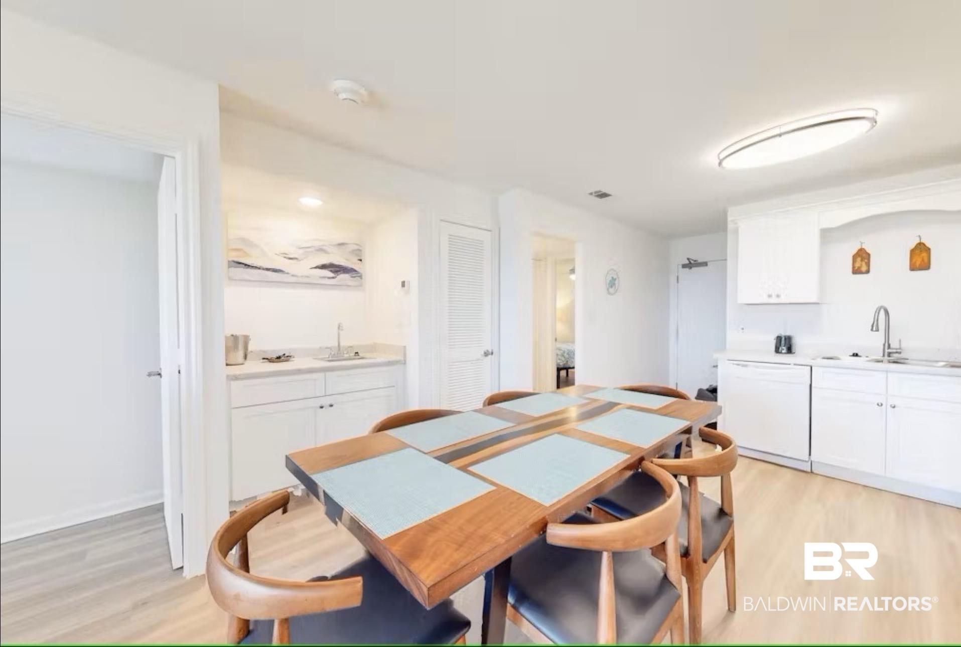 Image 4: Open-concept living space featuring wood-finish flooring, a contemporary dining area, and a functional wet bar with white cabinetry and a light-toned countertop