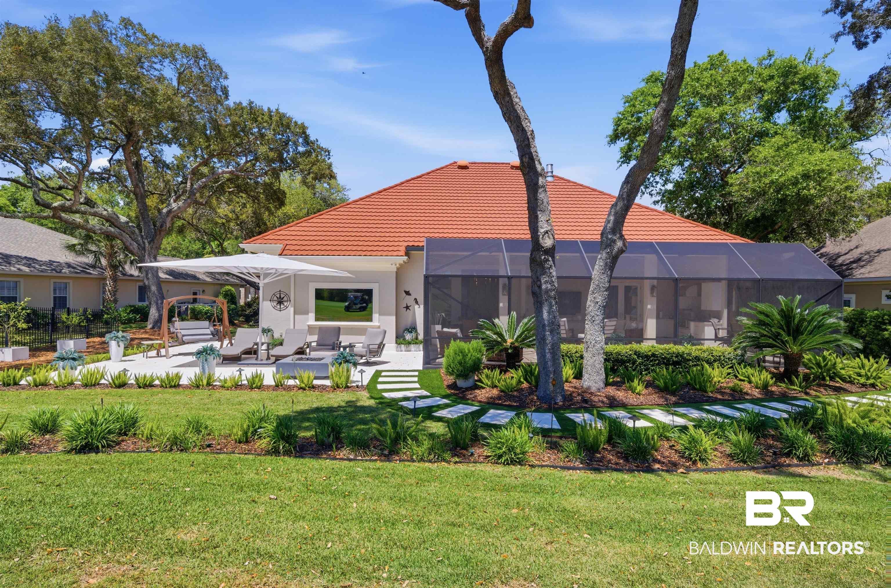 Image 2: Expansive rear patio featuring a large screened enclosure, tiled roof, mature landscaping, and square stepping stones