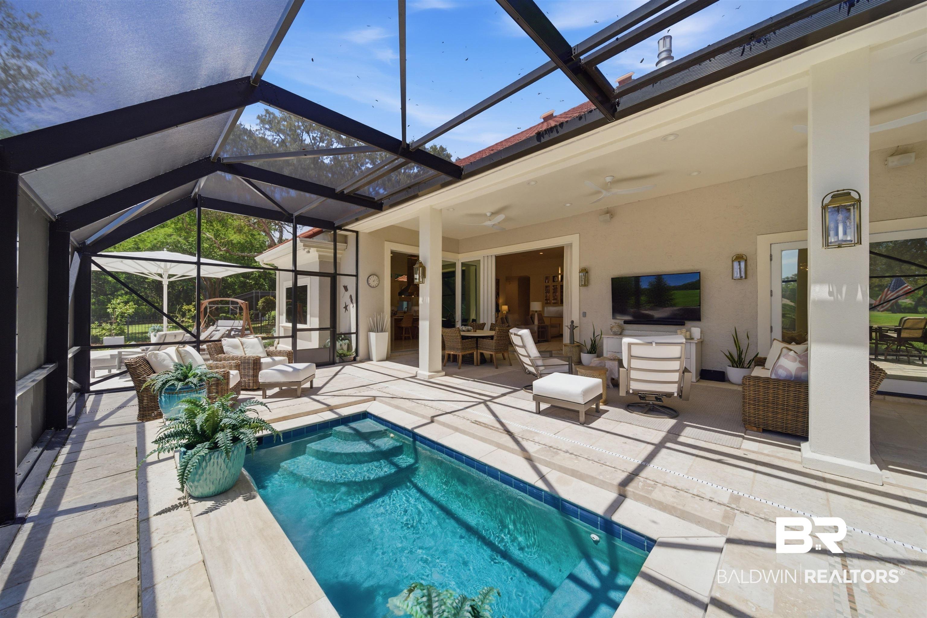 Image 4: Screened outdoor living area featuring a rectangular plunge pool with integrated steps, neutral-toned patio pavers, and a covered patio with ceiling fans and mounted exterior lighting