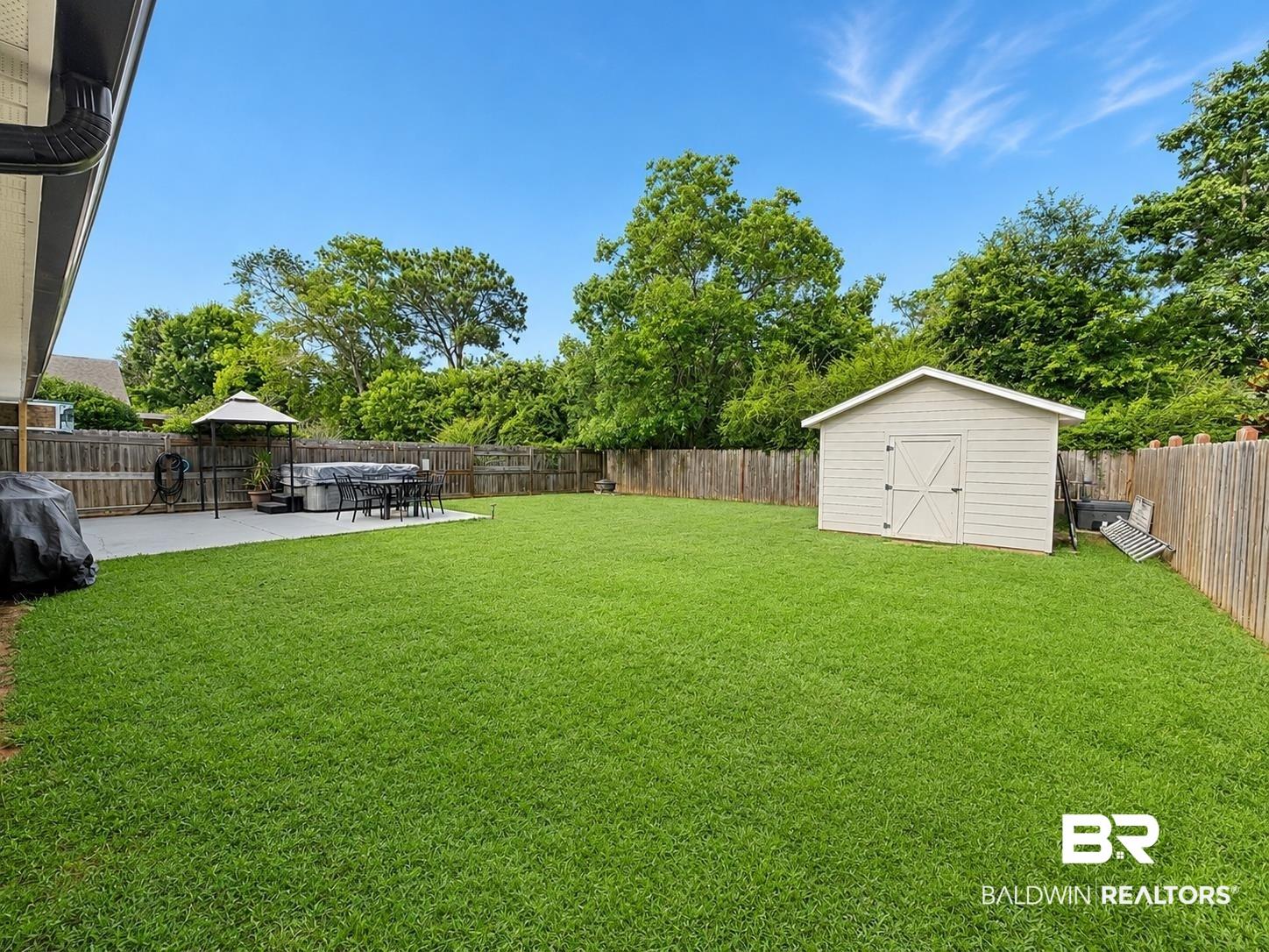 Image 2: Expansive backyard featuring a large green lawn, concrete patio, privacy fencing, and a detached storage shed