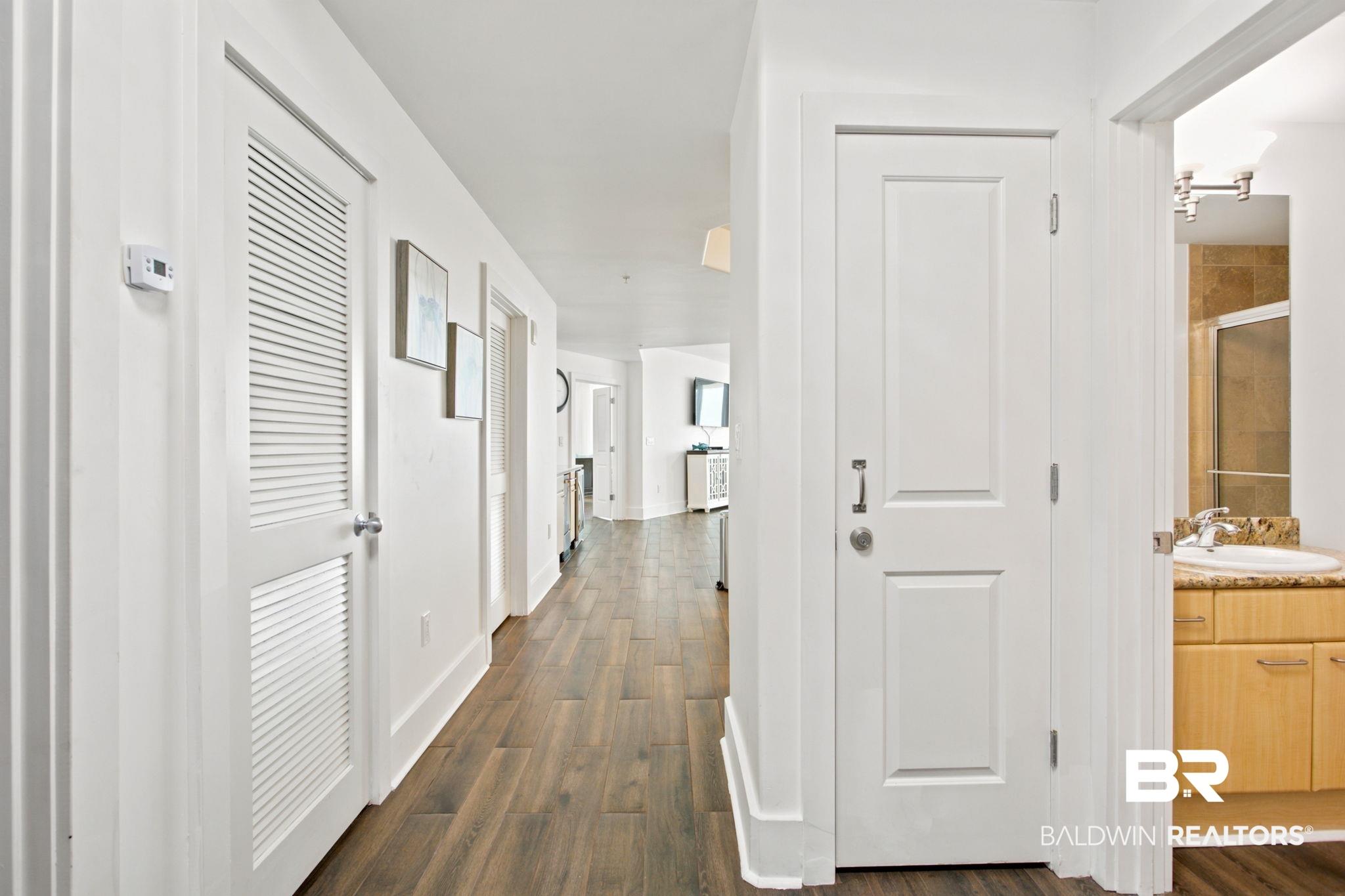 Image 3: Hallway featuring wood-finish flooring, white paneled doors, and contemporary wall art