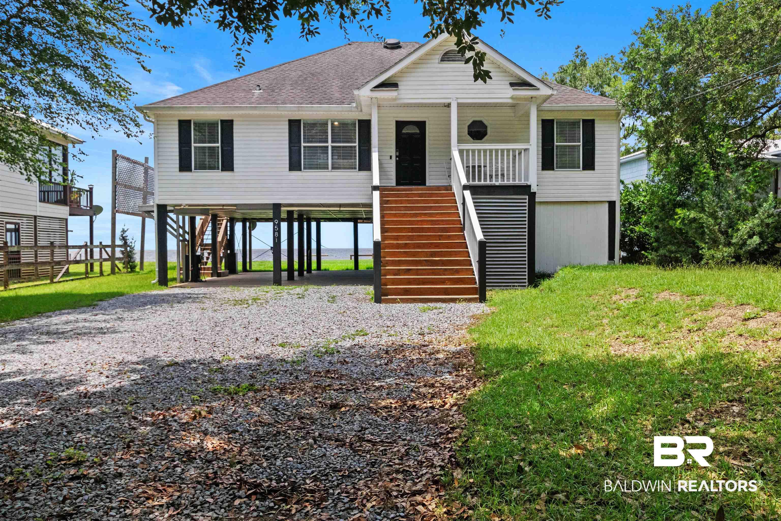 Image 4: Elevated coastal-style residence featuring white siding, a dark shingle roof, and black window shutters
