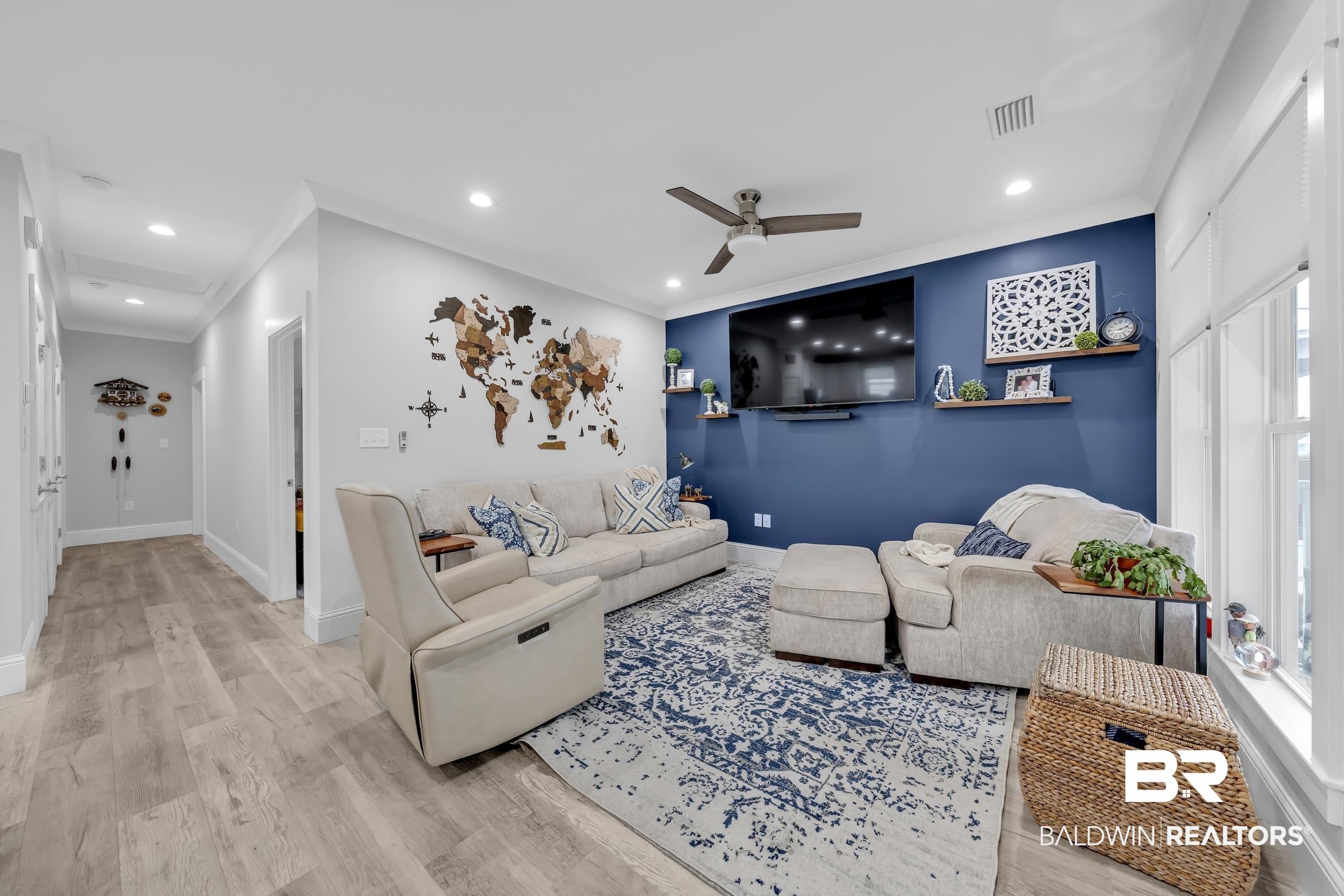 Image 4: Spacious living area featuring a prominent accent wall, wood-finish flooring, recessed lighting, and a ceiling fan