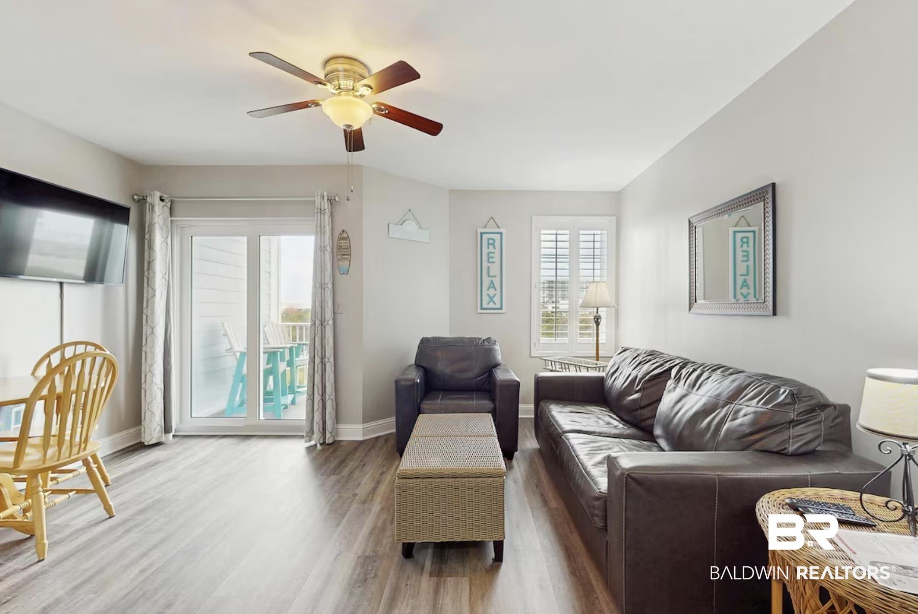 Image 2: Living area featuring wood-finish flooring, a ceiling fan with integrated lighting, and a wall-mounted television