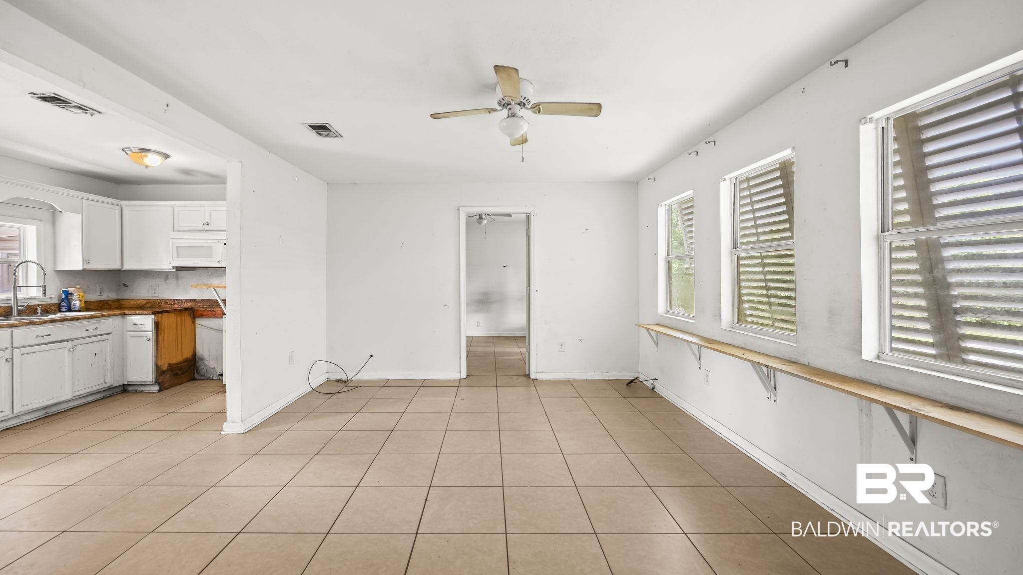 Image 4: Spacious living area featuring tile flooring, multiple windows, and a ceiling fan