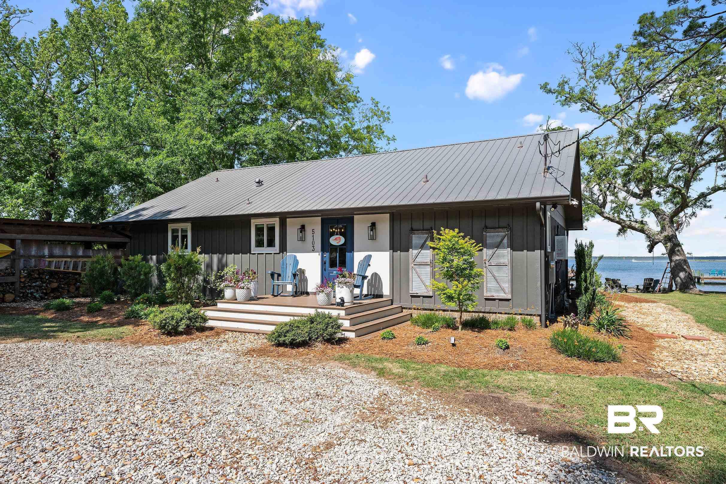 Image 2: Dark gray siding exterior with a metal roof, front porch, and water frontage