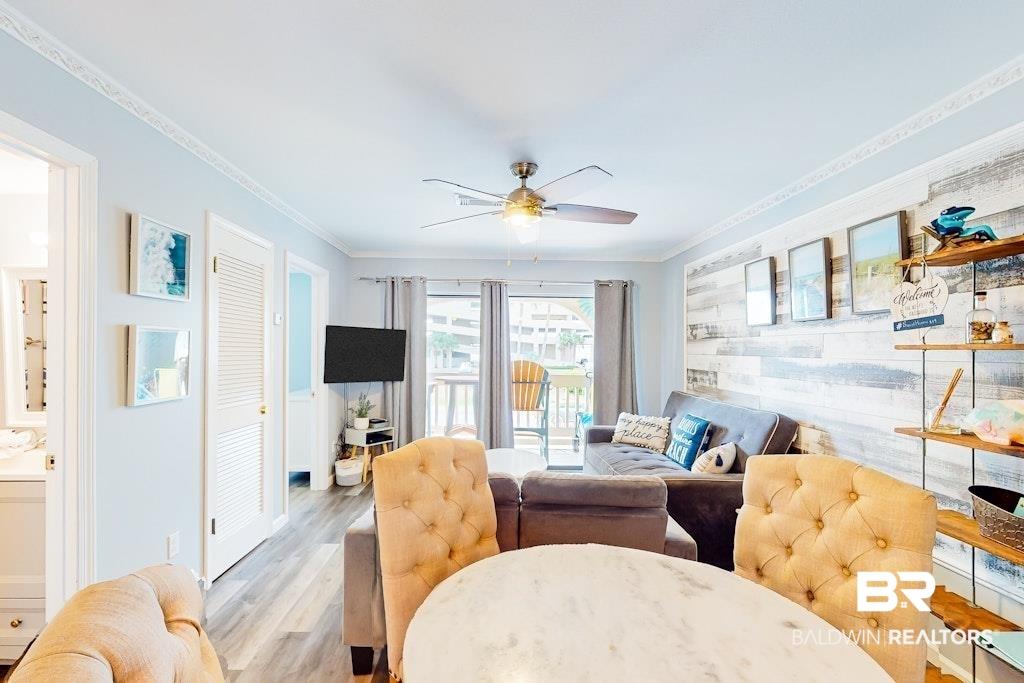 Image 4: Open-concept living area featuring wood-finish flooring, a decorative shiplap accent wall, and a ceiling fan with integrated lighting