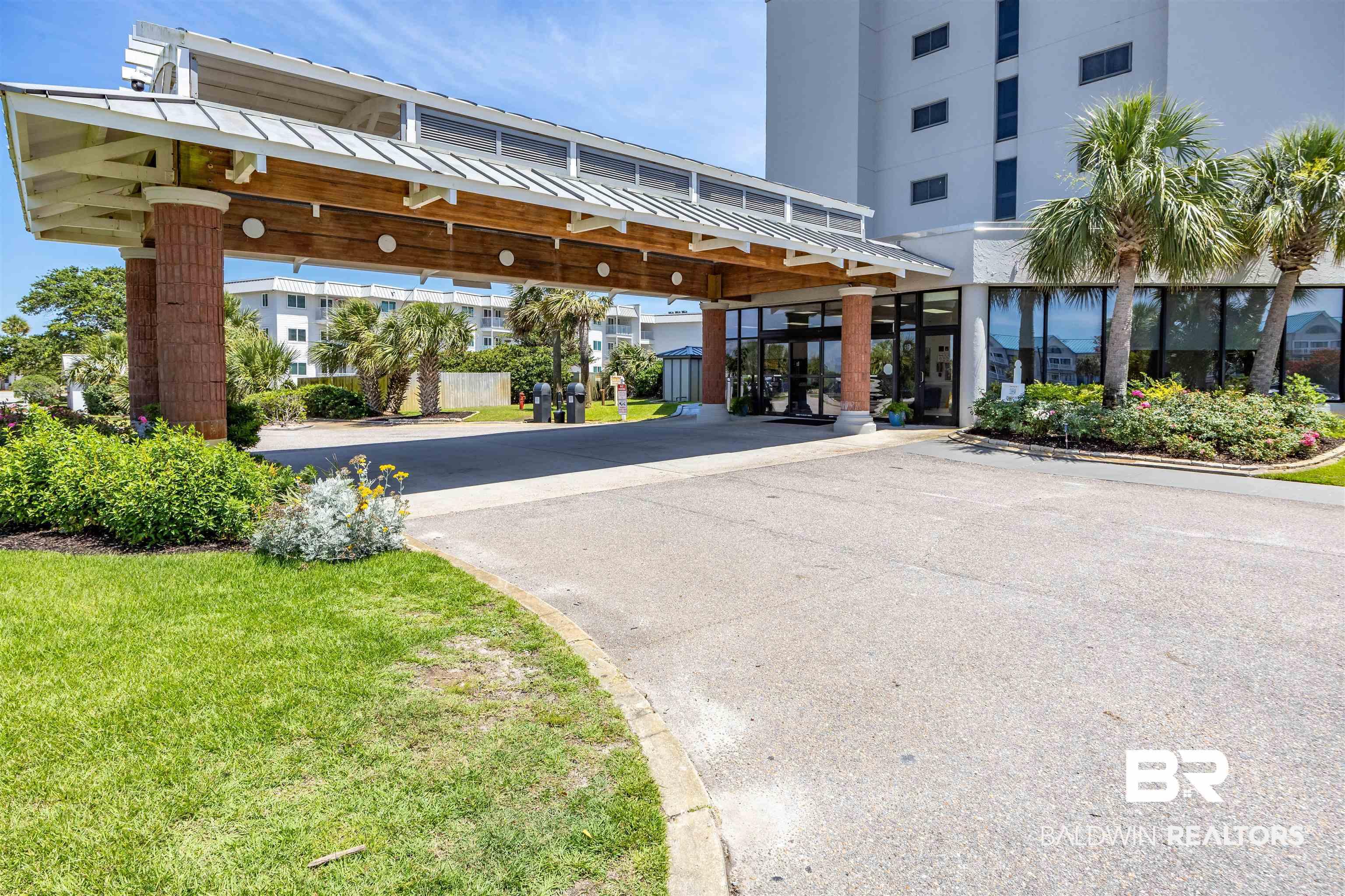 Image 4: Building entrance with a covered drive-through, glass double doors, brick-clad columns, and a white multi-story exterior