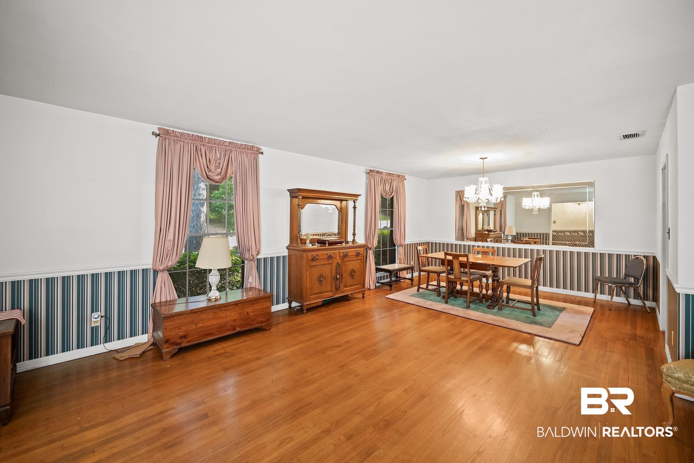 Image 3: Hardwood flooring spans this room, featuring multiple windows with natural light and a chandelier over the dining area