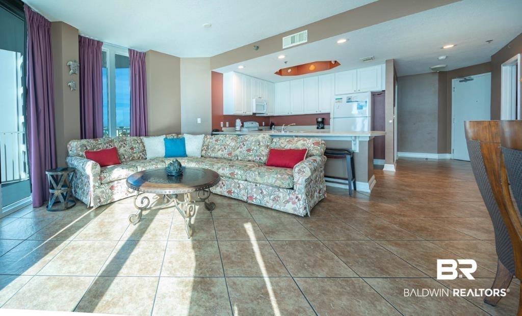 Image 3: Open-concept living space with tile flooring throughout, featuring a kitchen bar with seating, white cabinetry, and a full-height glass door
