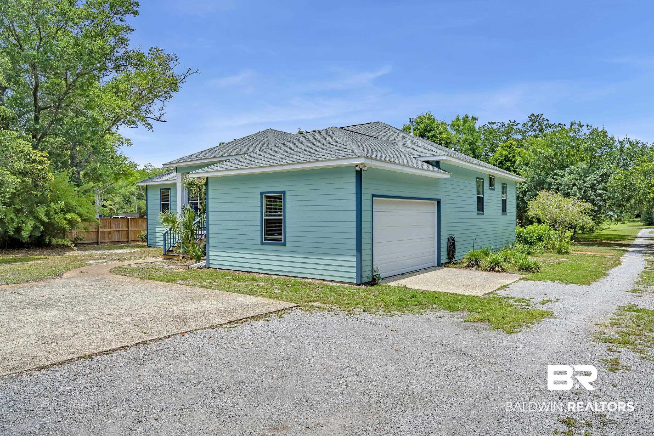 Image 4: Light blue siding exterior with a white garage door, featuring a concrete driveway and gravel parking area