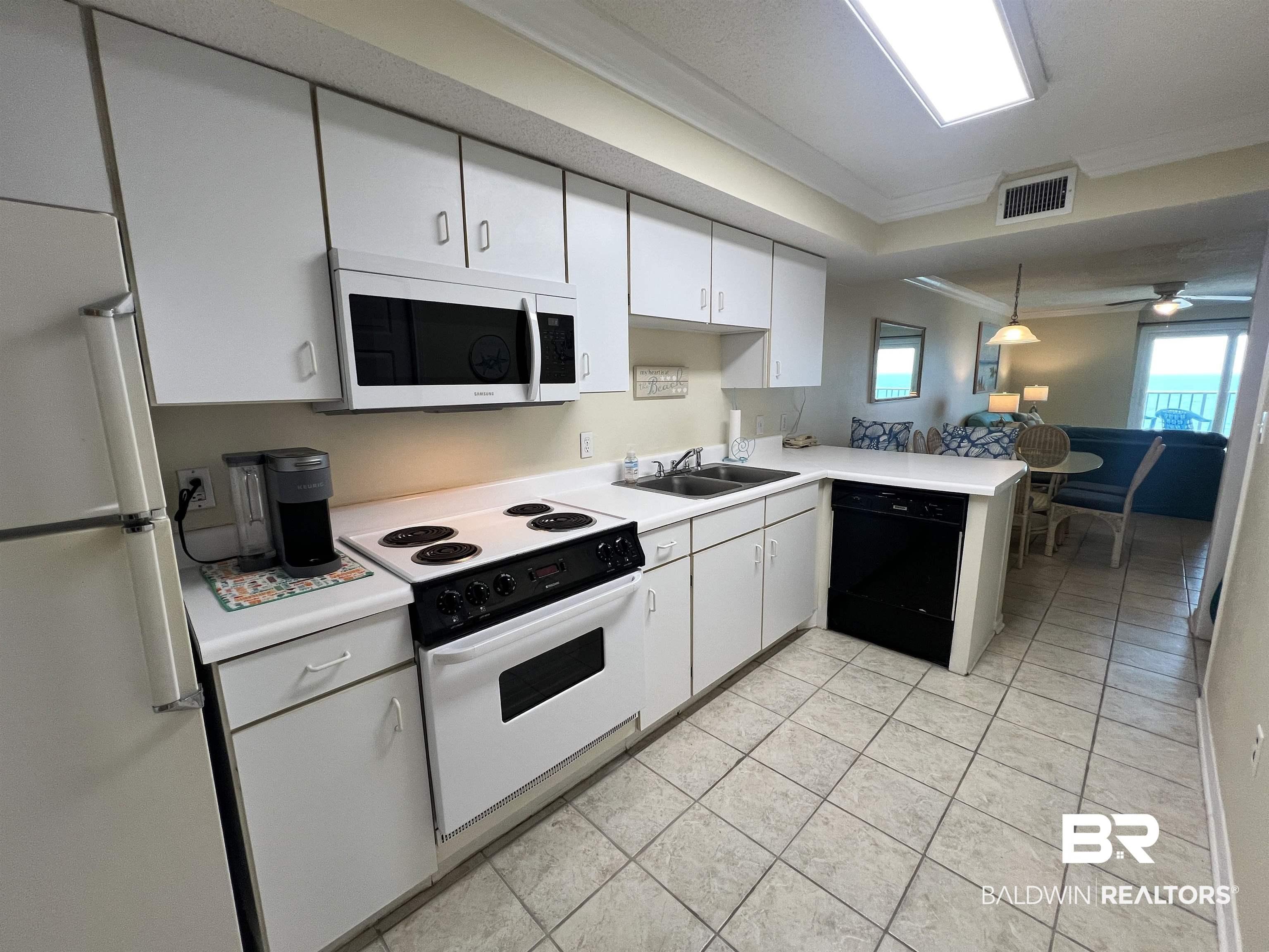 Image 3: Efficient kitchen featuring white cabinetry, a built-in microwave, a flat-top stove, and a double basin sink
