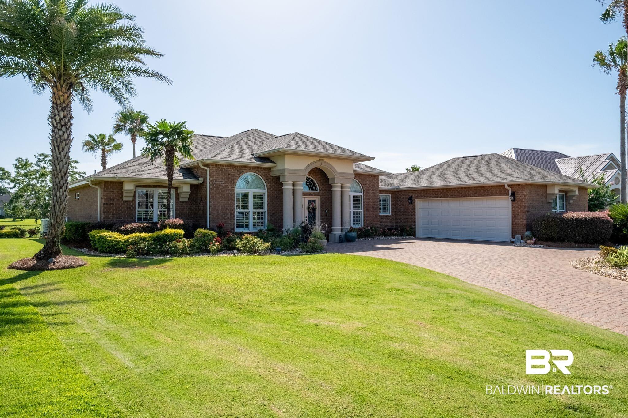 Image 2: Brick exterior featuring an arched portico with columns, a paver driveway, an attached garage, mature palm trees, and manicured landscaping