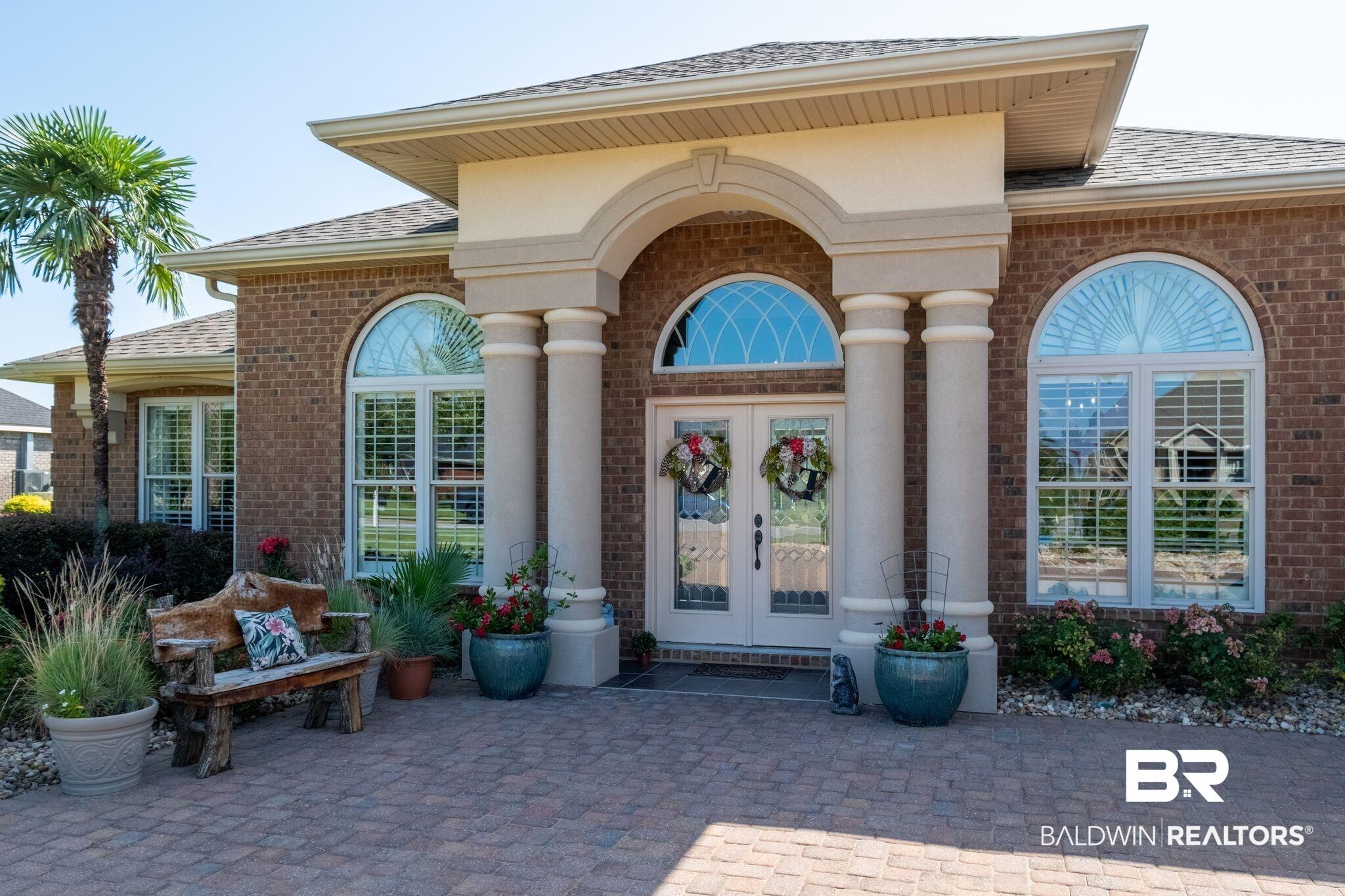 Image 4: Brick exterior featuring a portico entry with double columns, arched transom windows, double glass-paneled entry doors, and a paver stone patio