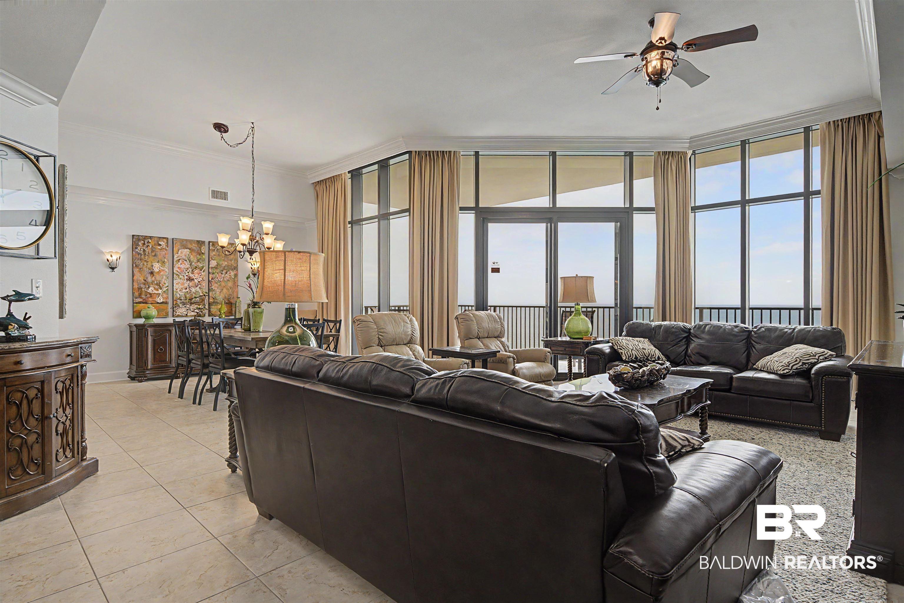 Image 3: Expansive living area featuring floor-to-ceiling windows, a glass-paneled door opening to a balcony, tile flooring, and a dining area with a multi-arm chandelier
