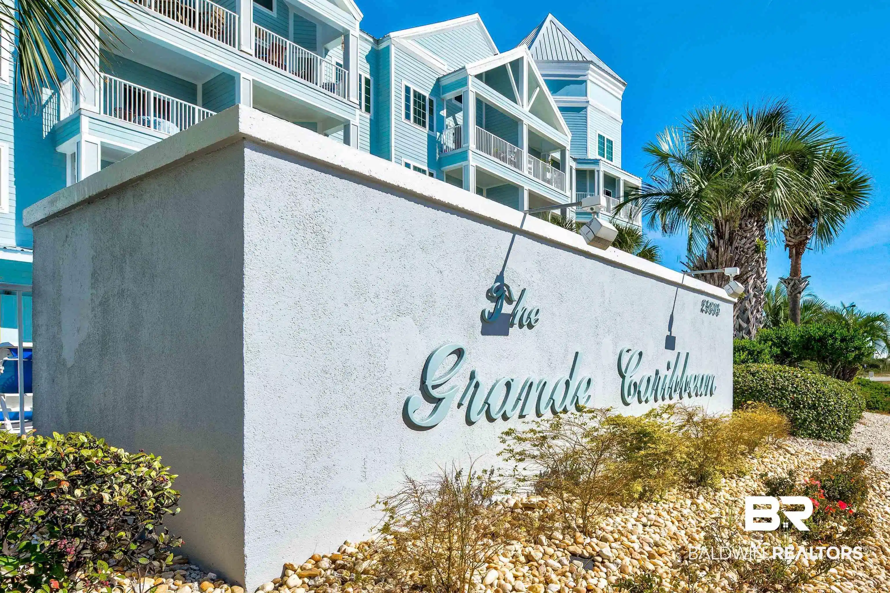Image 1: Stucco wall with "The Grande Caribbean" signage, surrounded by gravel ground cover and established landscaping