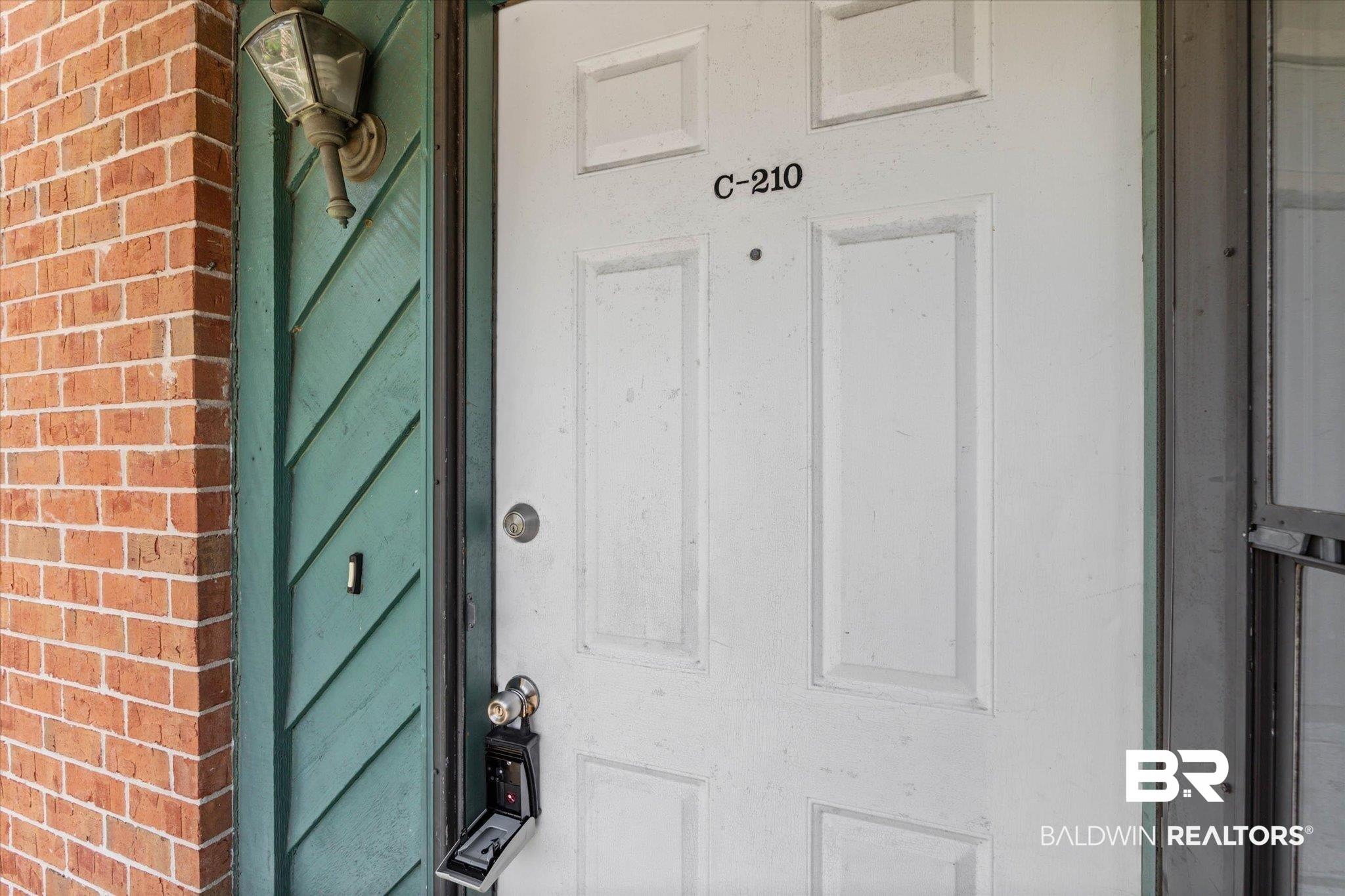 Image 2: White paneled entry door with unit number C-210, complemented by a decorative wall-mounted lantern light fixture