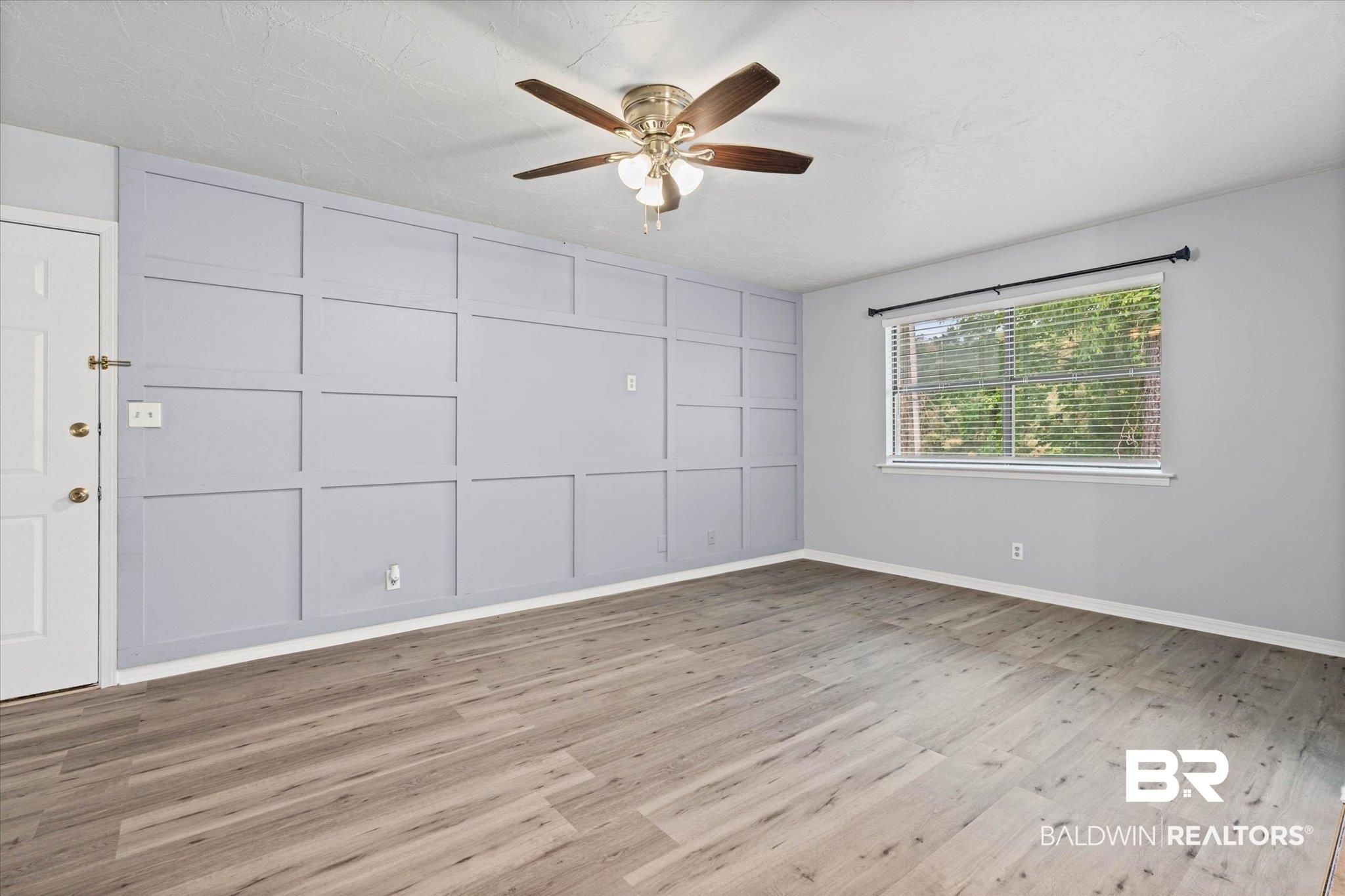 Image 4: Spacious room featuring a decorative accent wall, wood-finish flooring, and a ceiling fan with integrated lighting