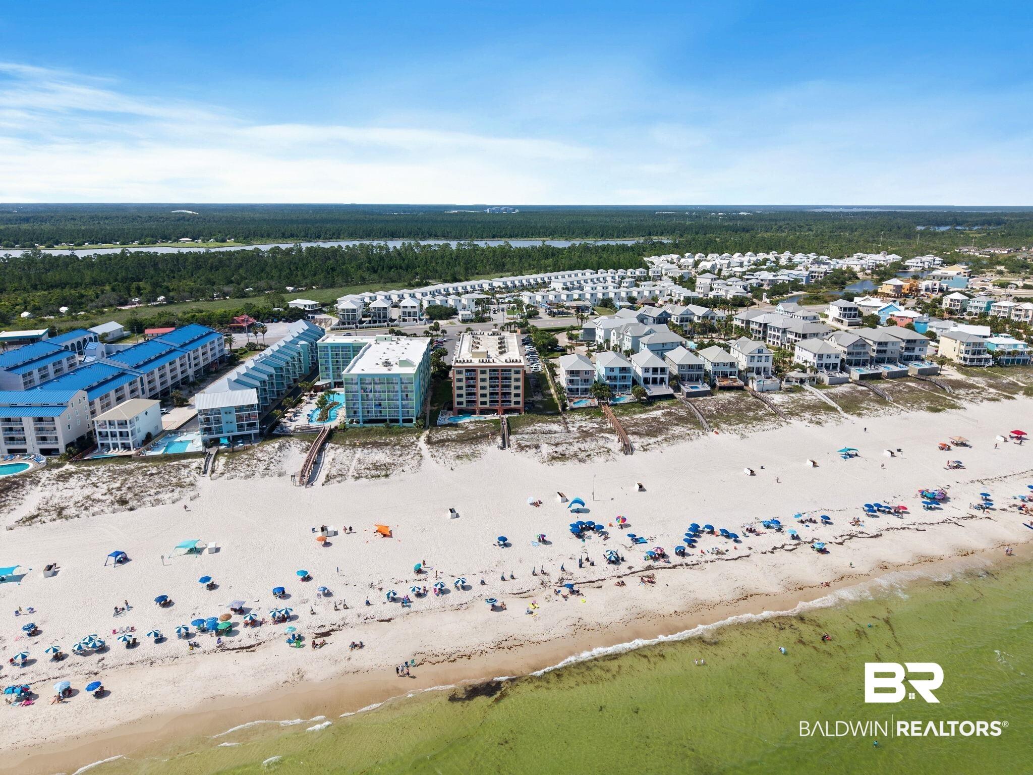 Image 3: Expansive sandy beach with clear green water, bordered by multiple residential properties and resort-style buildings