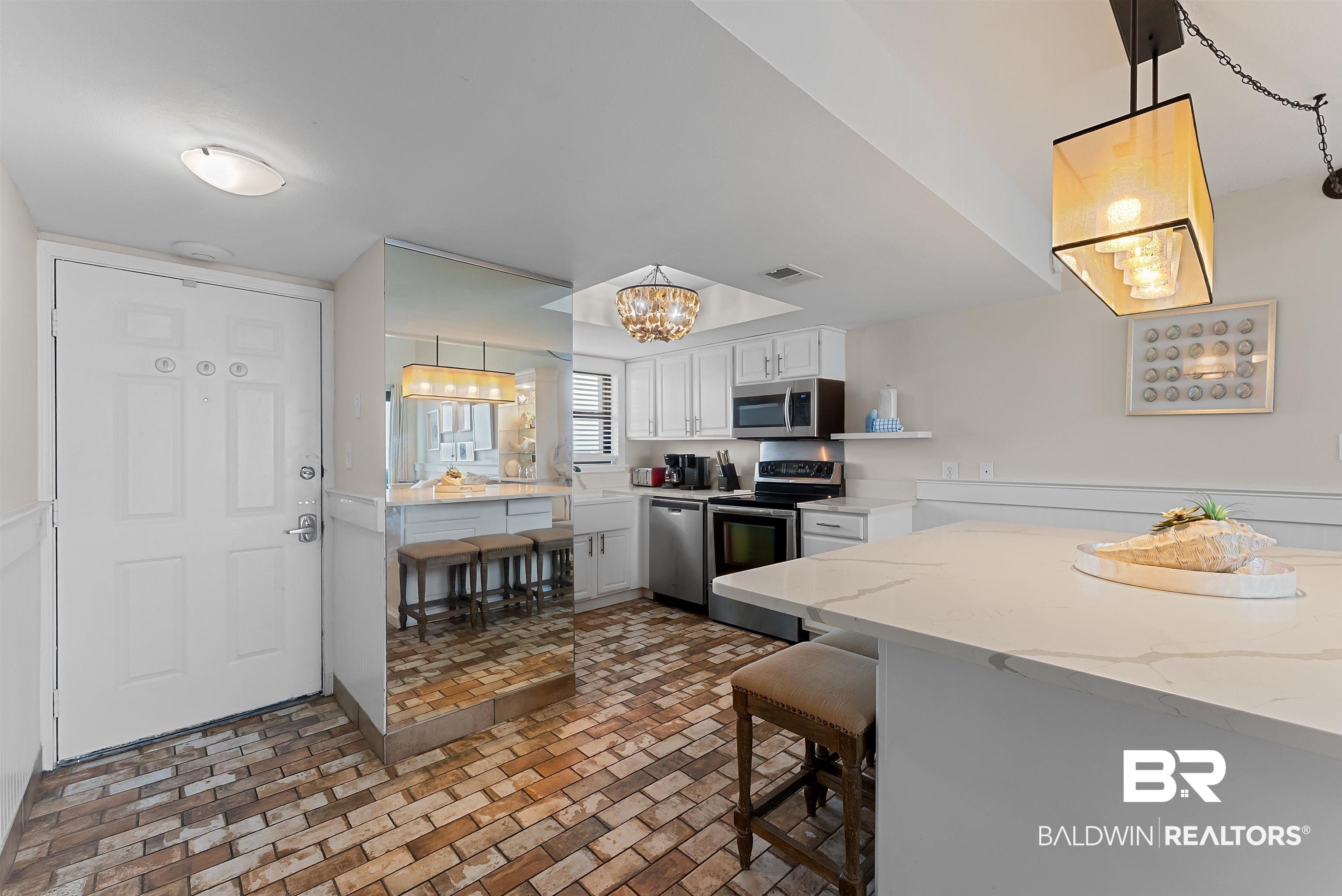 Image 4: Kitchen featuring white cabinetry, stainless steel appliances, a white island with a countertop, and brick-patterned flooring