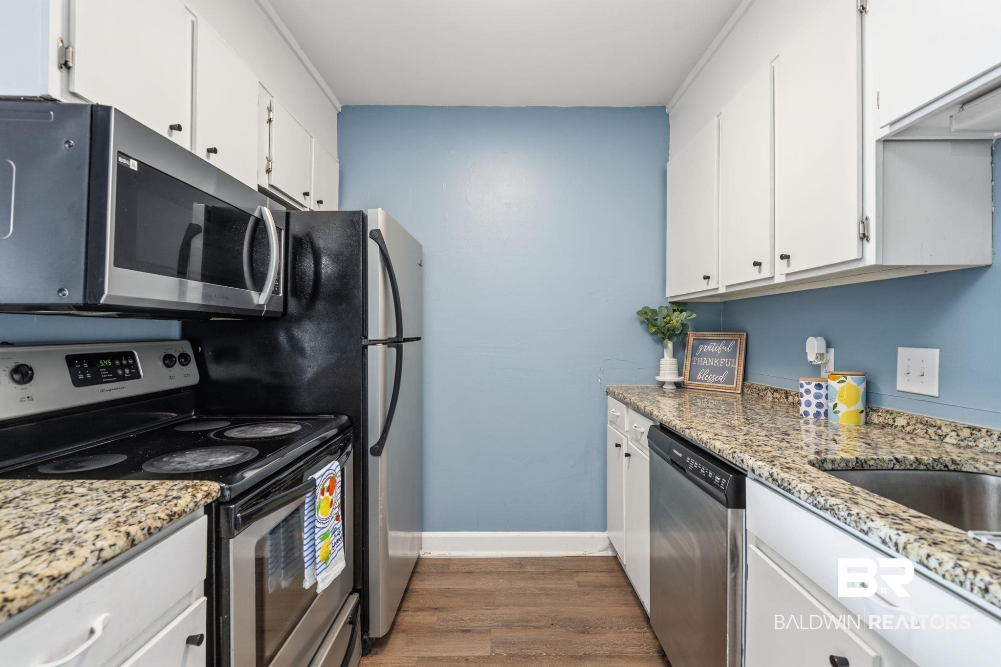 Image 3: Compact kitchen featuring white cabinetry, wood-finish flooring, and light-colored granite countertops