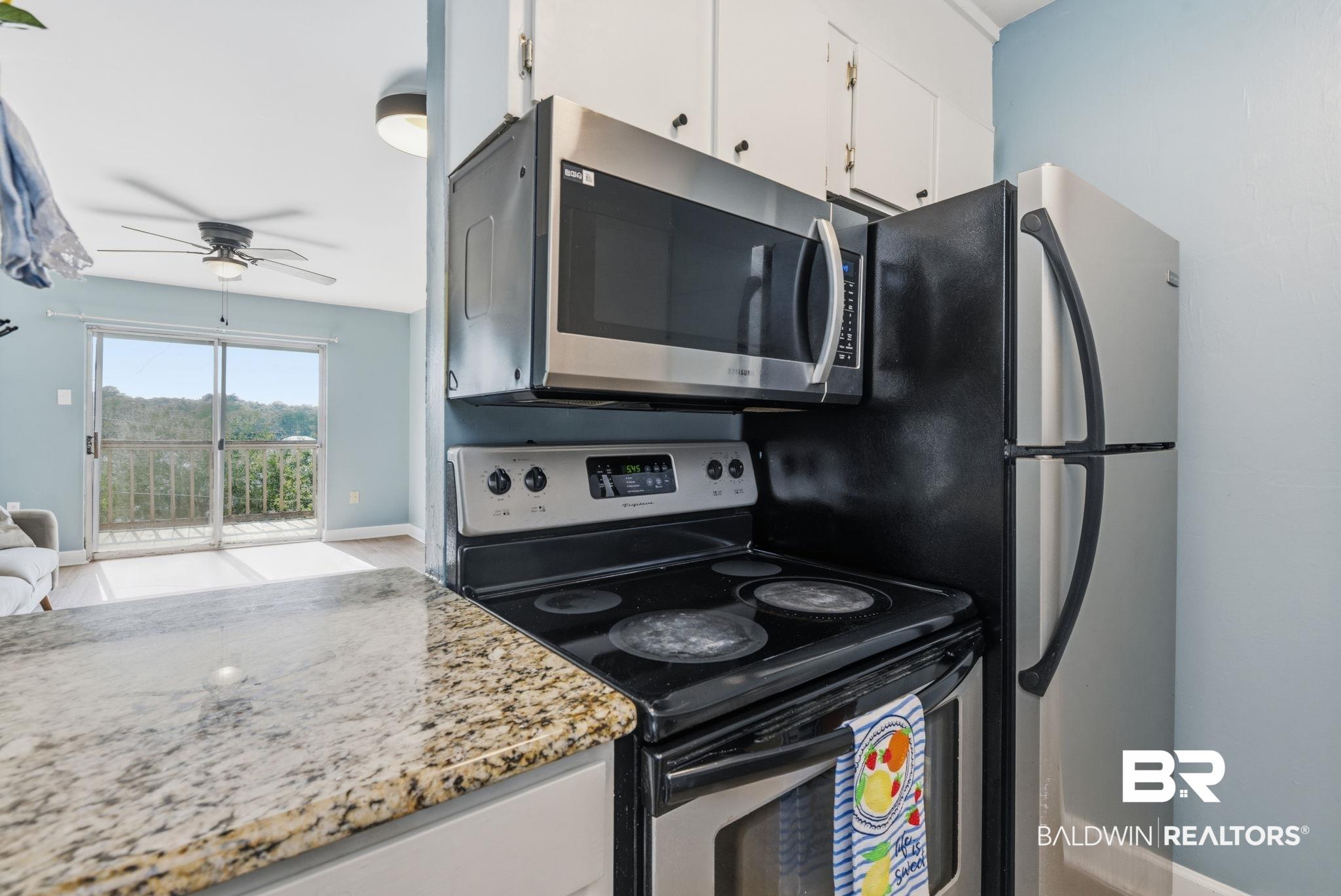 Image 4: Kitchen featuring a granite-style countertop, stainless steel appliances including an over-the-range microwave, and light-toned cabinetry
