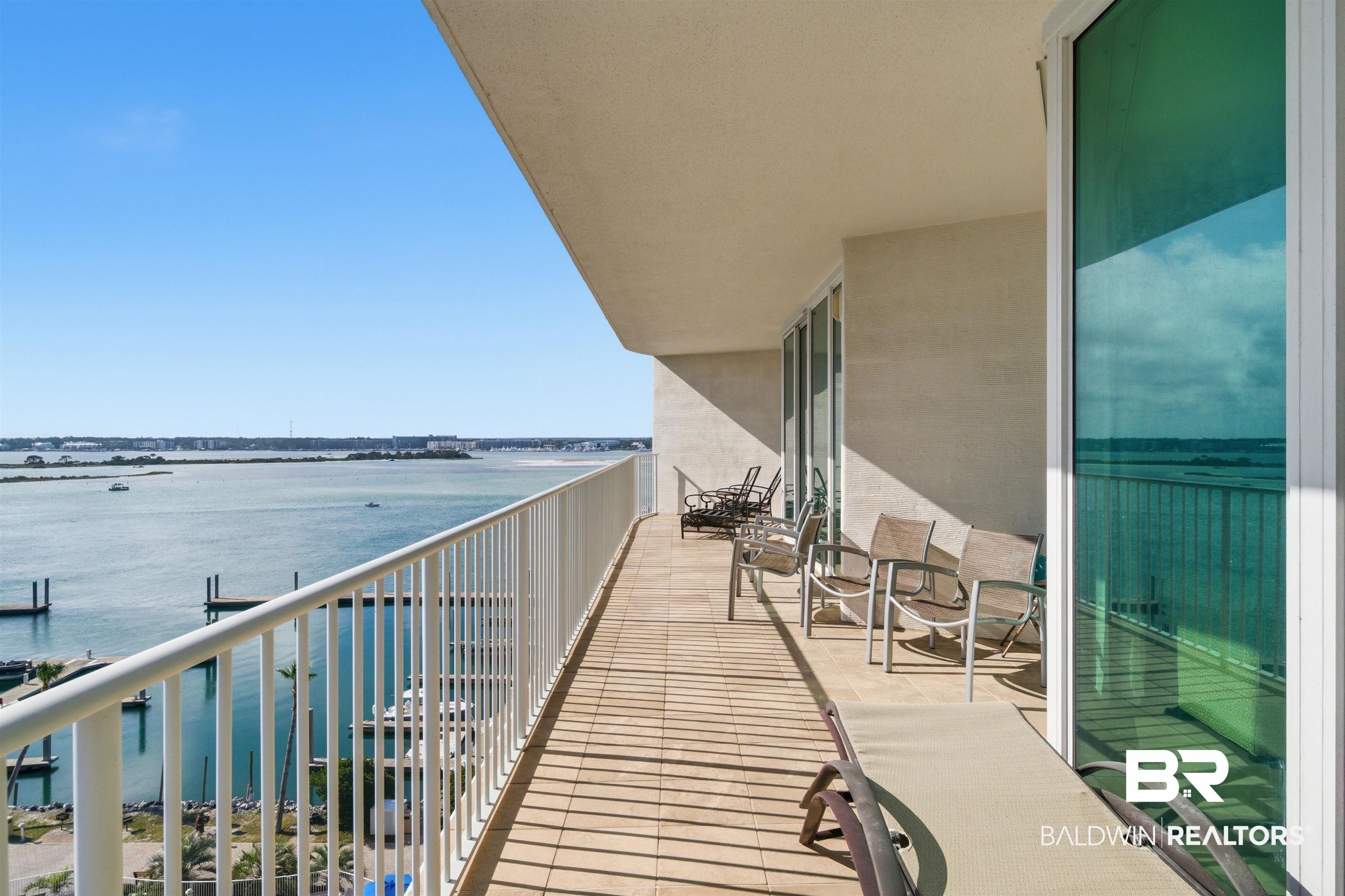 Image 3: Expansive balcony featuring water frontage, white railing, floor-to-ceiling glass sliding doors, and light-toned tile flooring